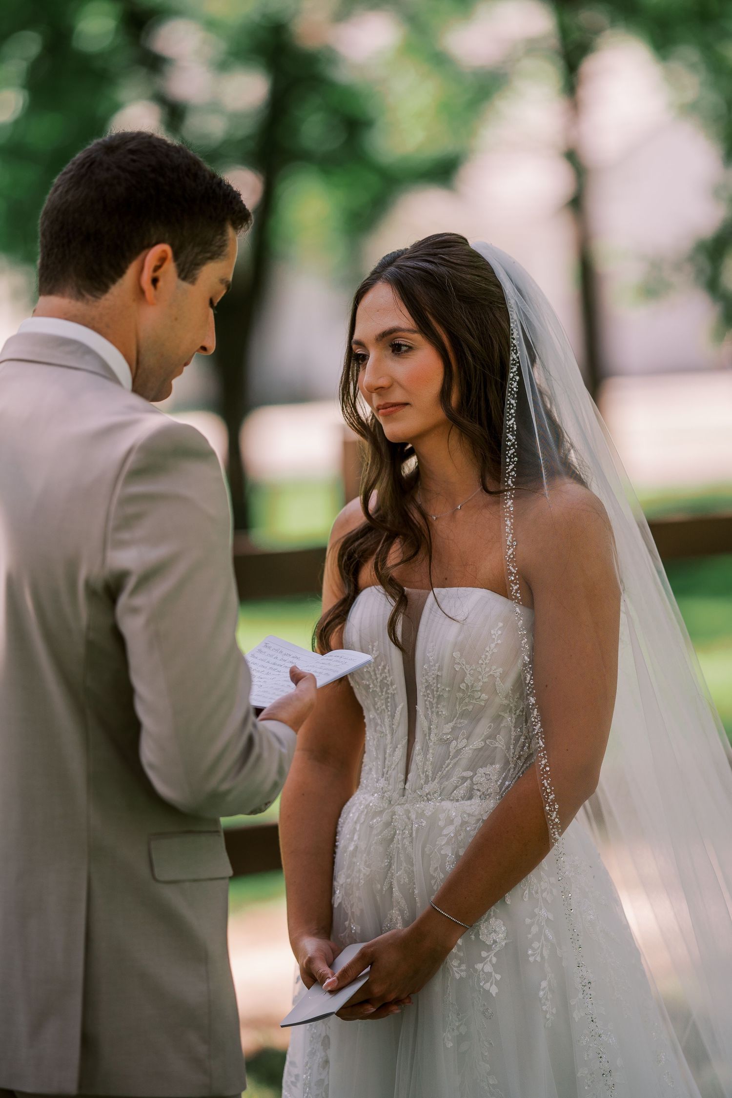 A couple exchanges vows during an intimate outdoor wedding ceremony with a bride wearing a white lace gown and veil.