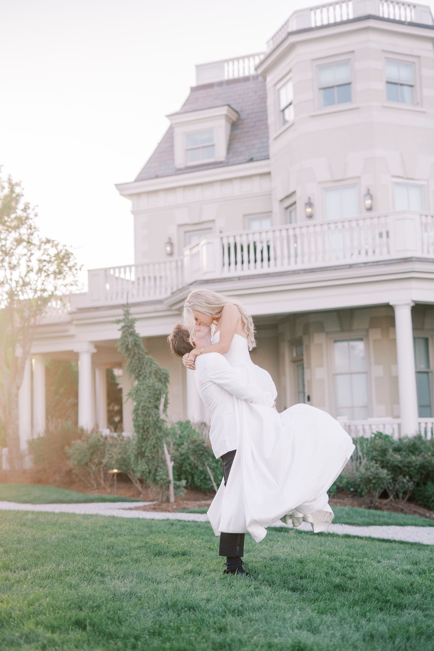 A romantic wedding scene on a mansion lawn with elegant architecture and soft natural lighting in the background.