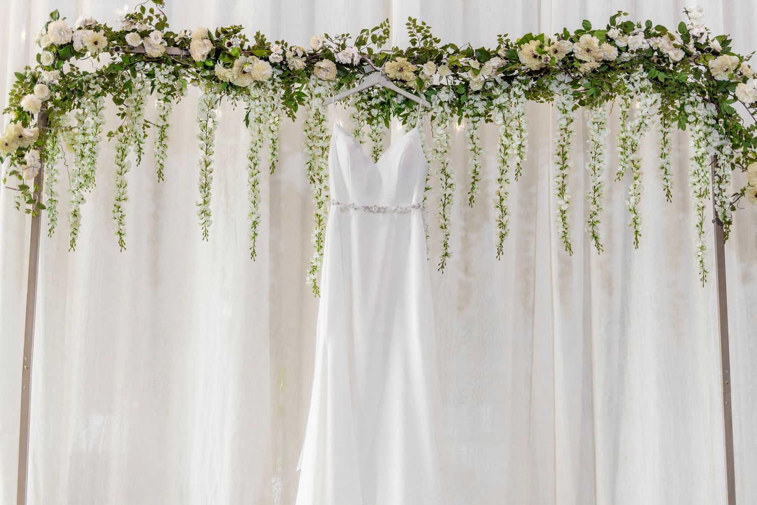 A garden-inspired wedding backdrop with cascading white florals, greenery and sheer white fabric draping.