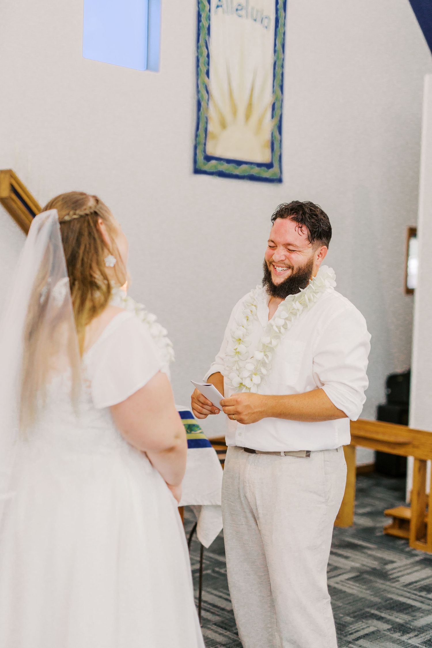 A couple exchanges rings during their wedding ceremony while wearing traditional white attire.