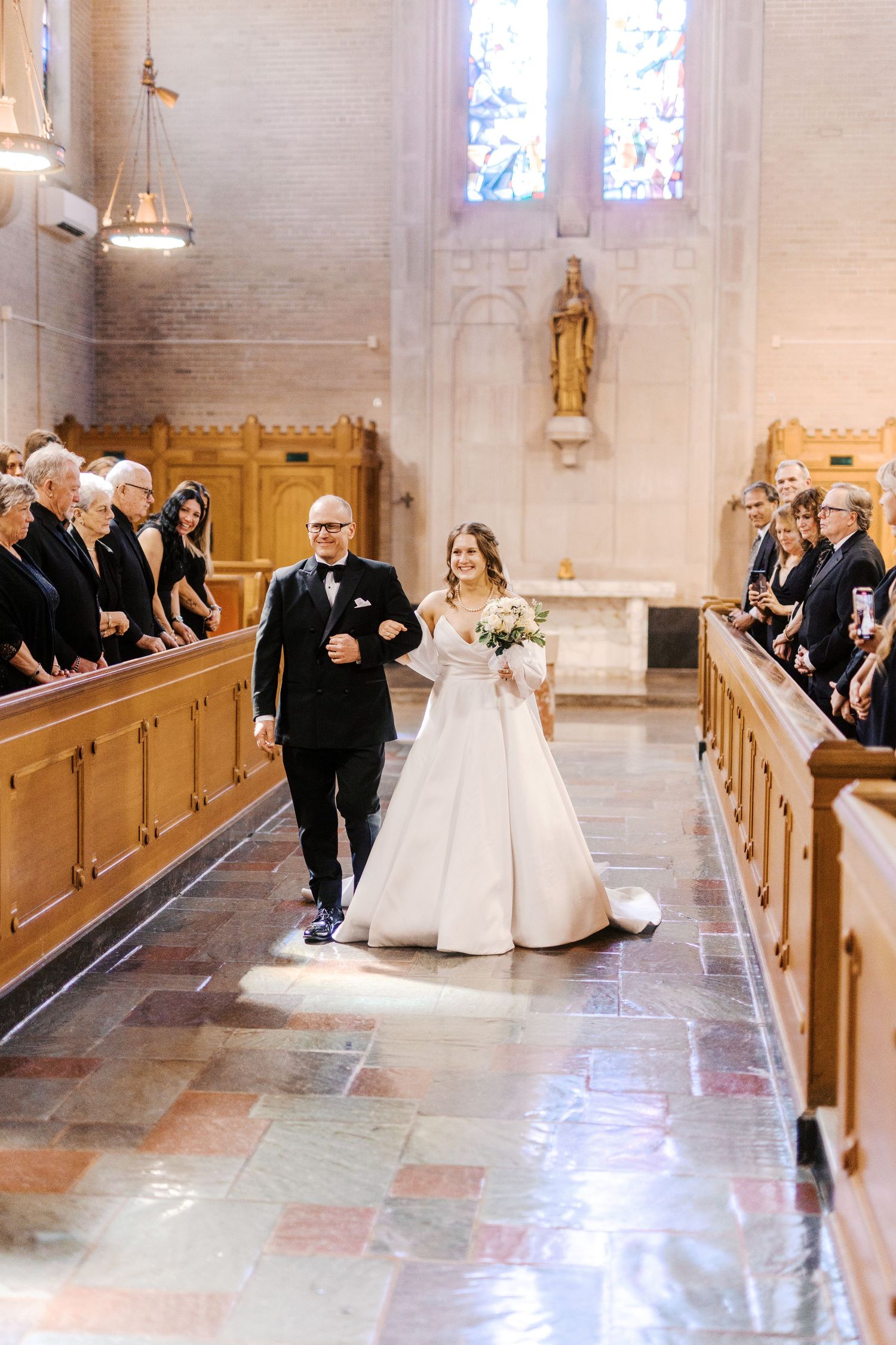 A wedding procession walking down the church aisle as guests look on from wooden pews.