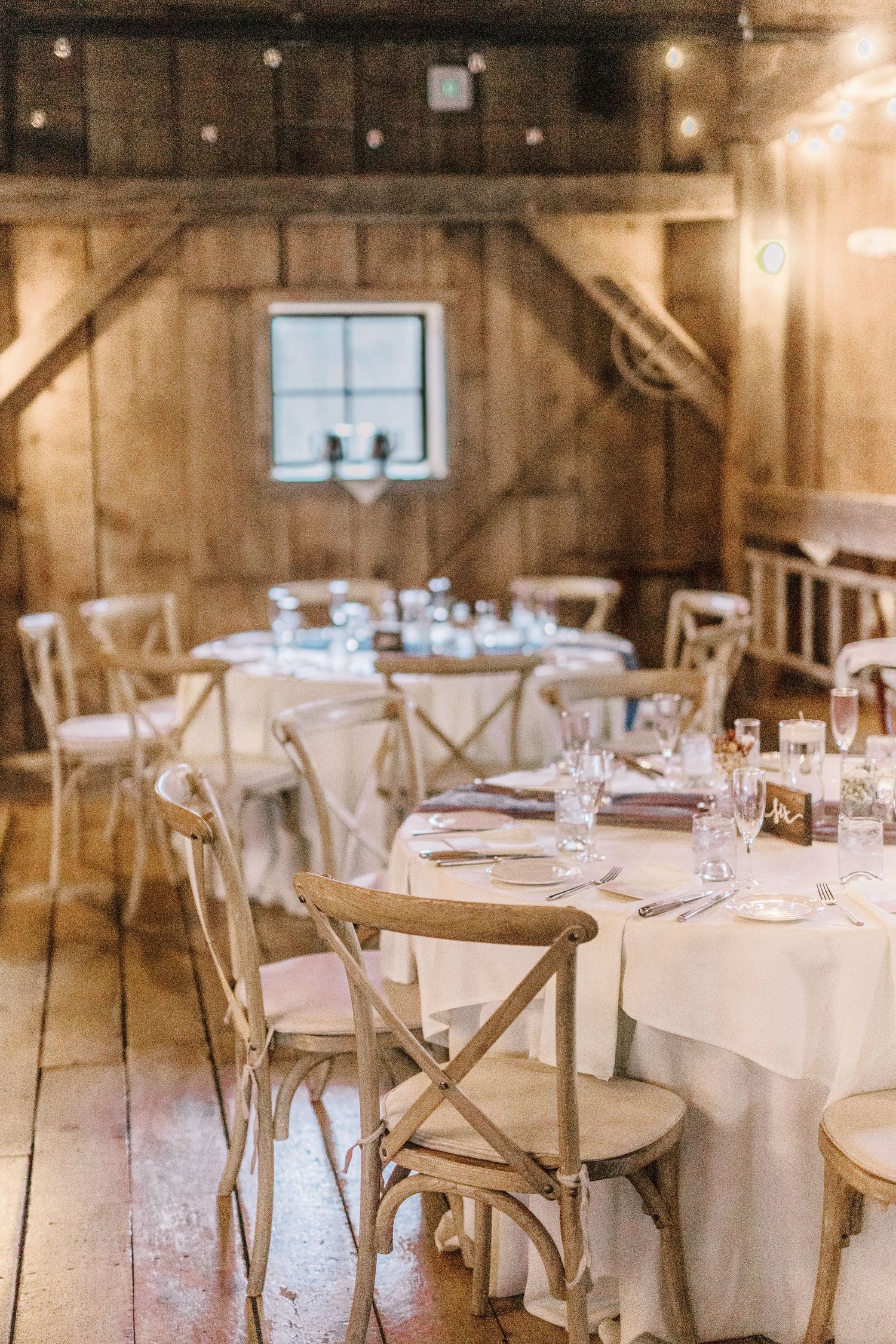 Rustic barn wedding reception venue with elegant table settings and cross-back chairs.