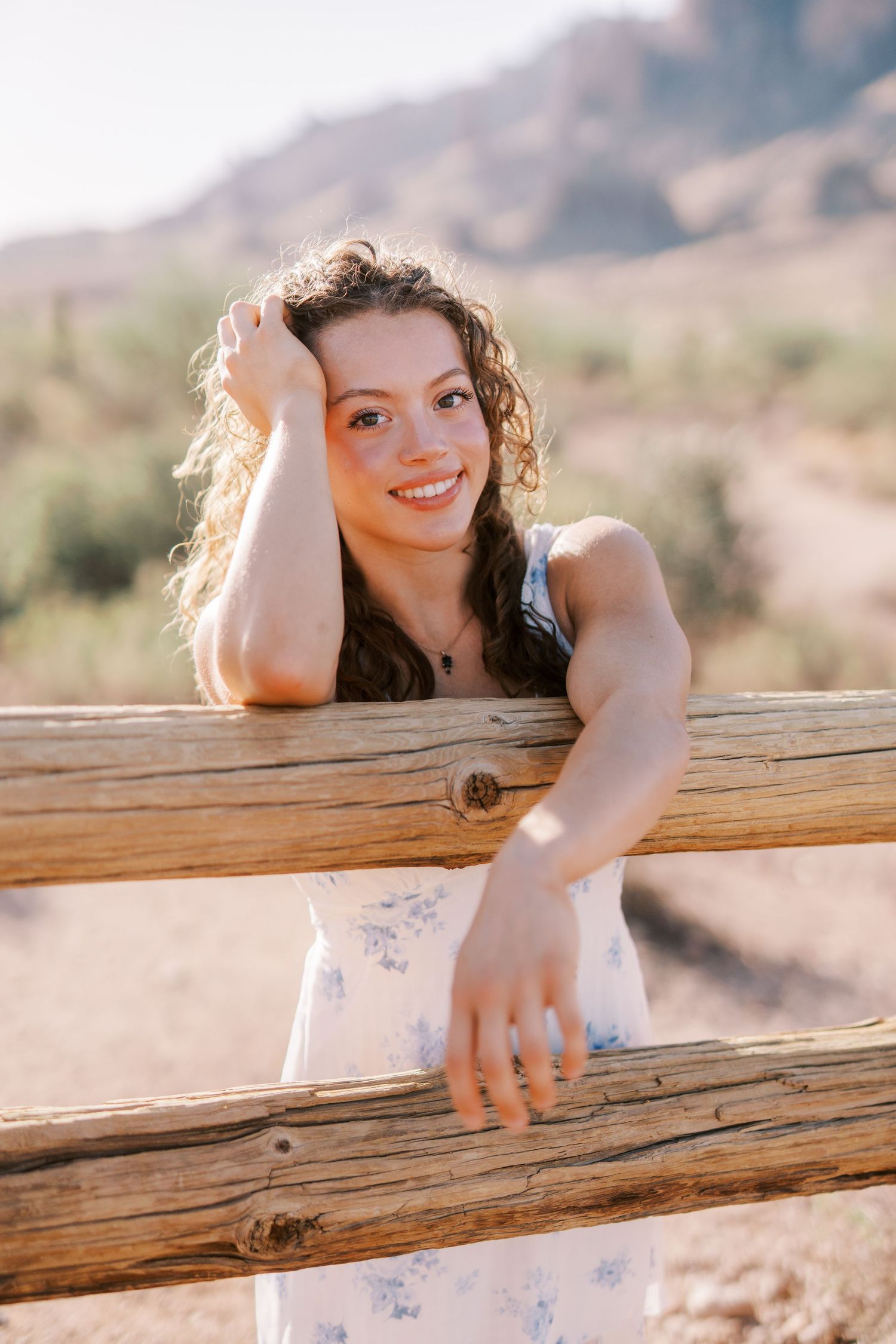 Portrait of someone leaning on wooden fence rails in desert landscape at golden hour with mountains in background.