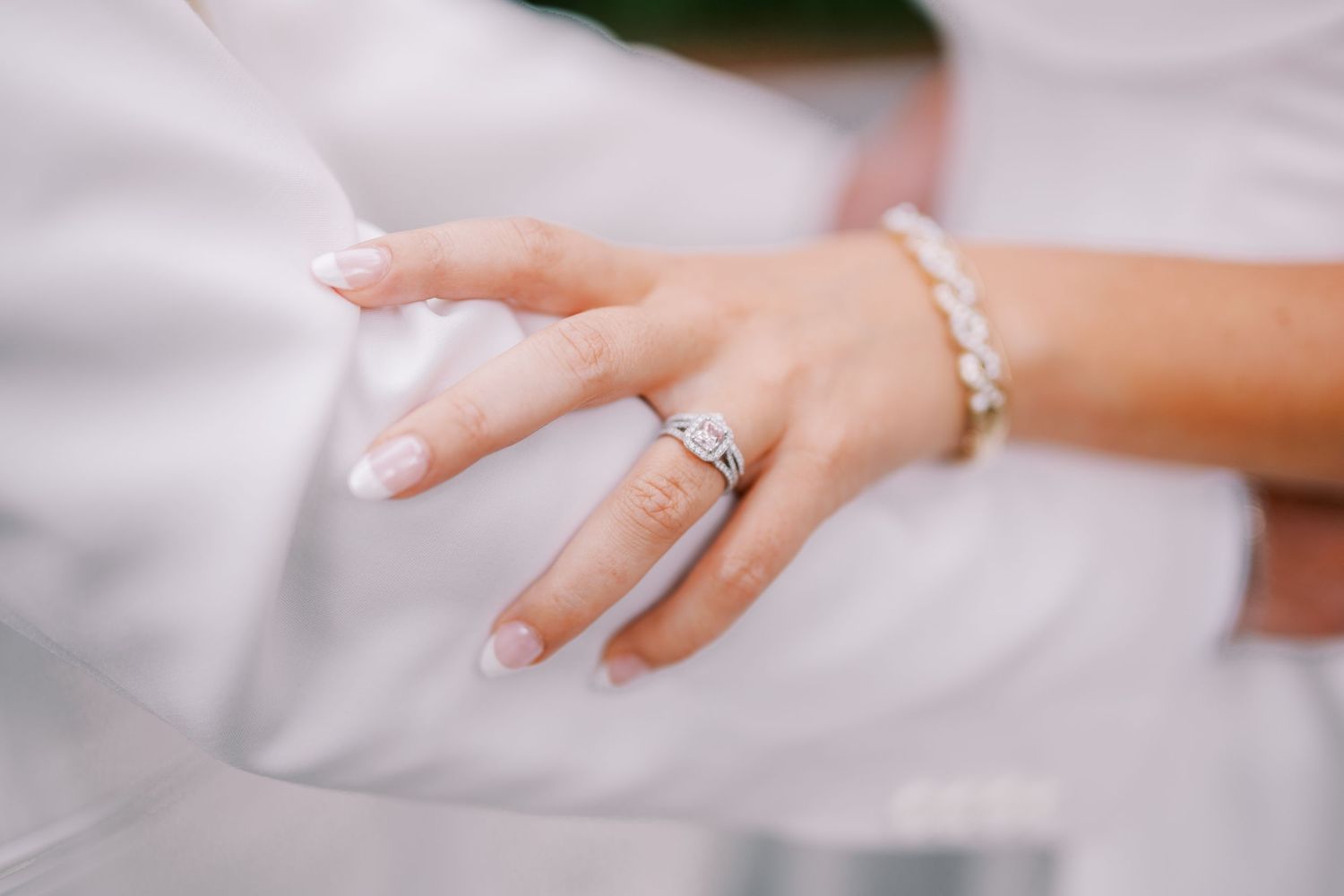 A close-up view of multiple hands wearing diamond engagement rings against a soft white background.