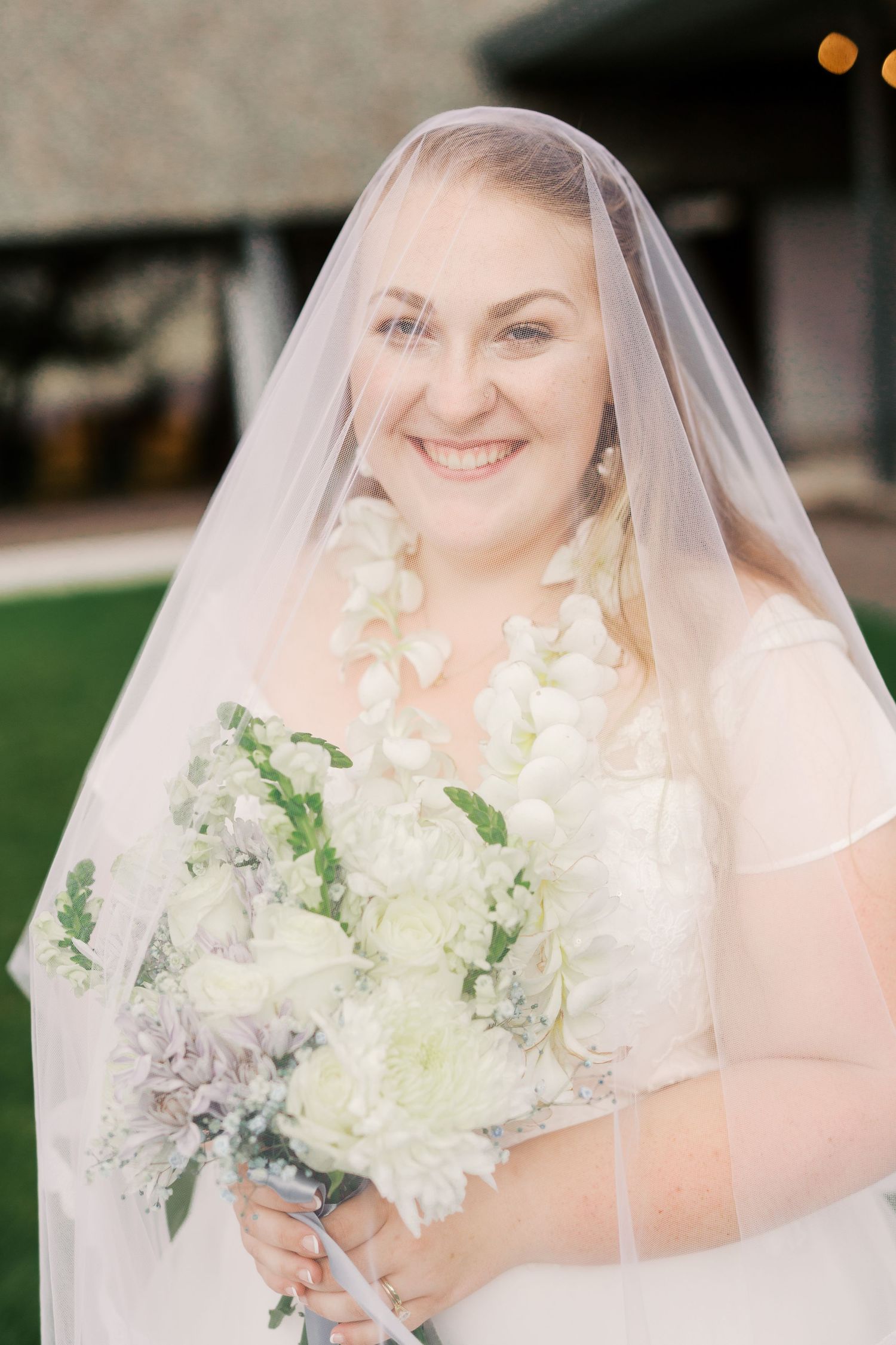A radiant bride in a white gown and veil holding a bouquet of white flowers.