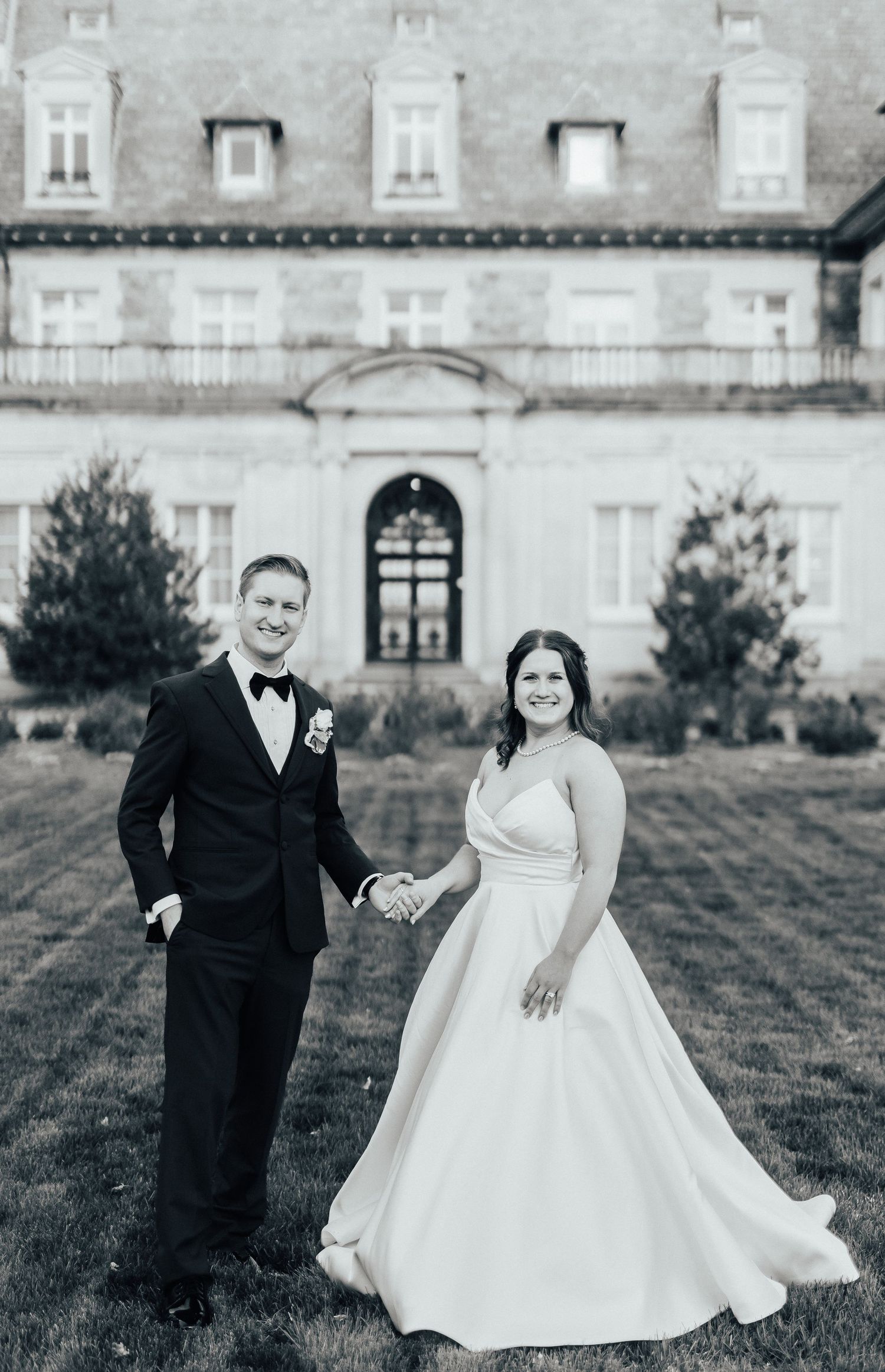 Newlyweds pose together on mansion grounds in classic black and white photography style.