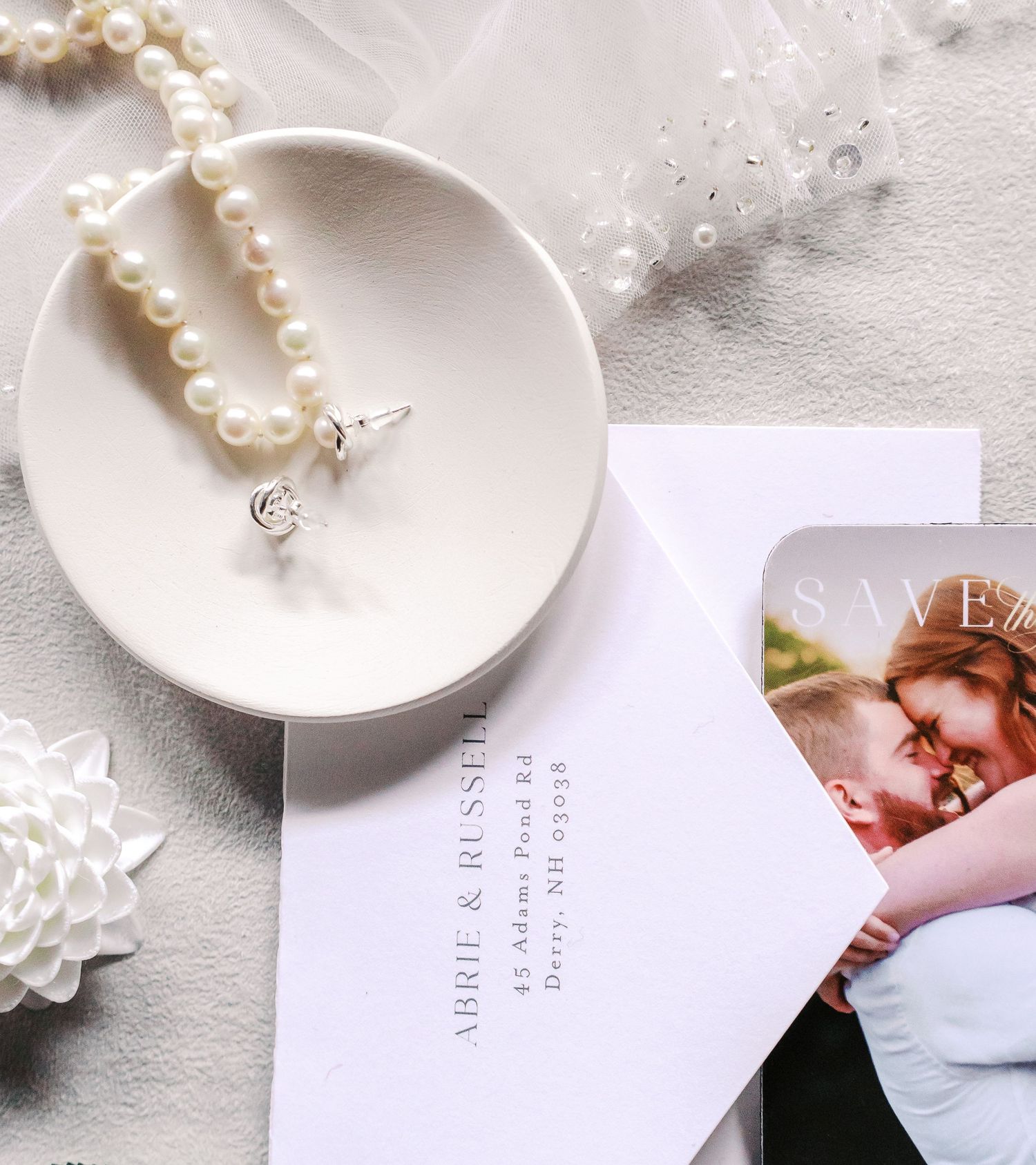 A pearl necklace and wedding invitation styled on a white ceramic dish with delicate details.