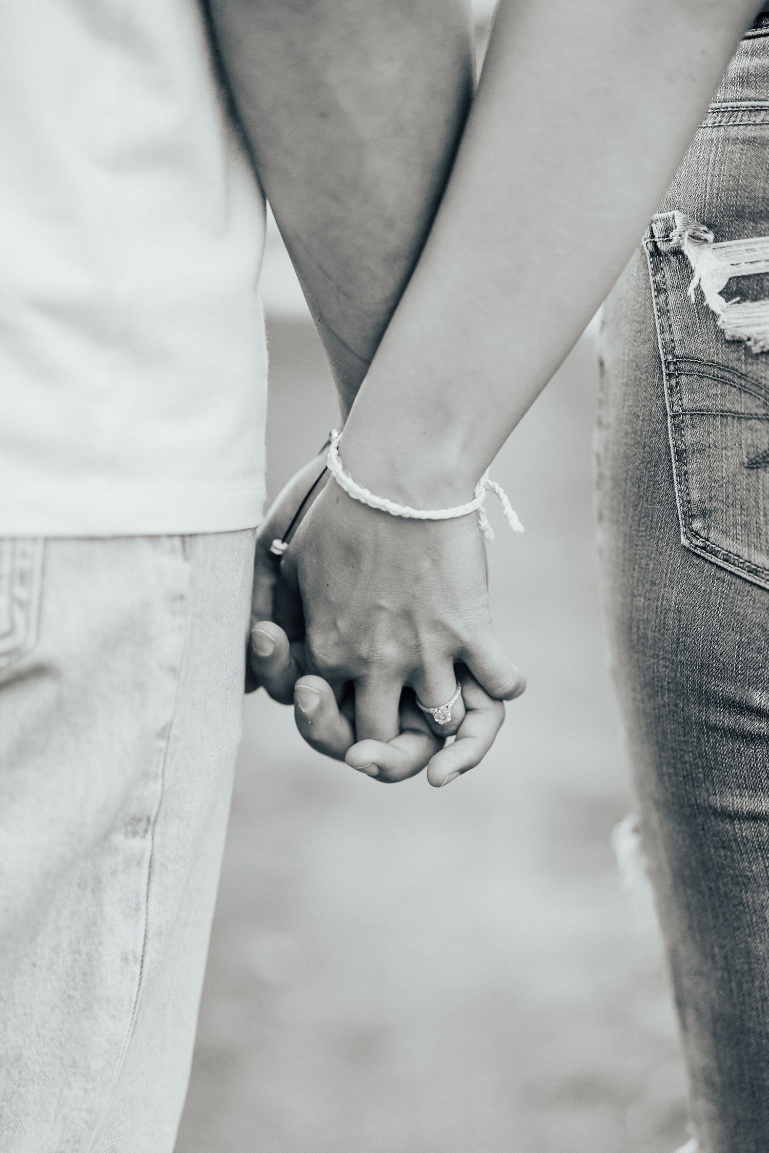 Black and white detail shot of a couple holding hands with matching friendship bracelets.