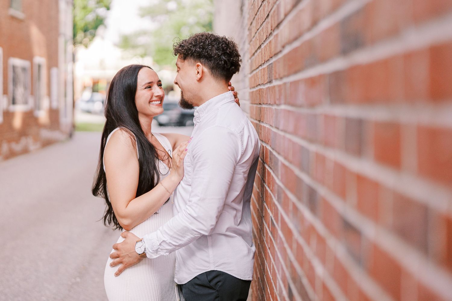A couple shares an intimate moment together against a brick wall on a city sidewalk.