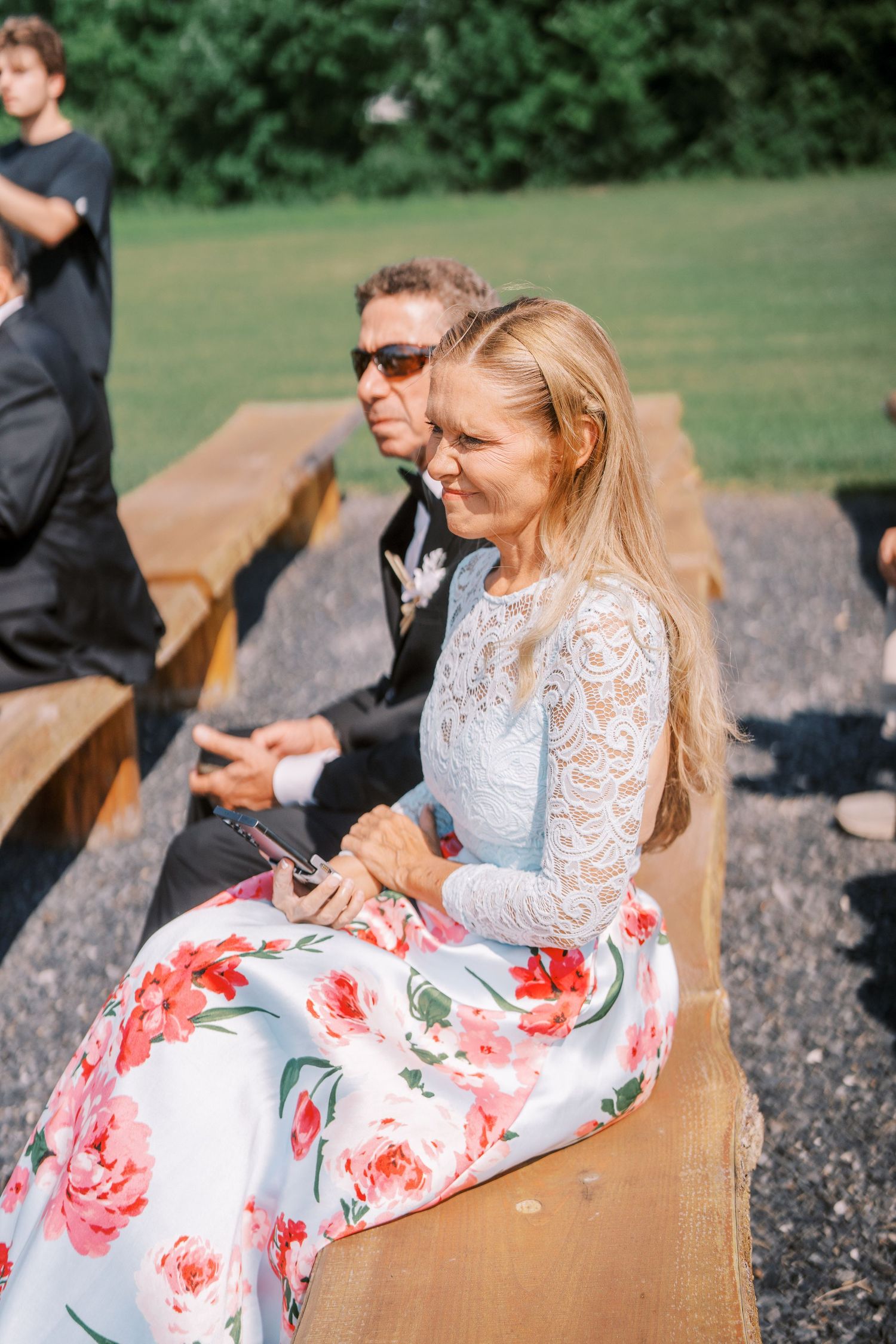 A couple sitting outdoors at a rustic picnic table, with person wearing a lace top and floral print skirt.