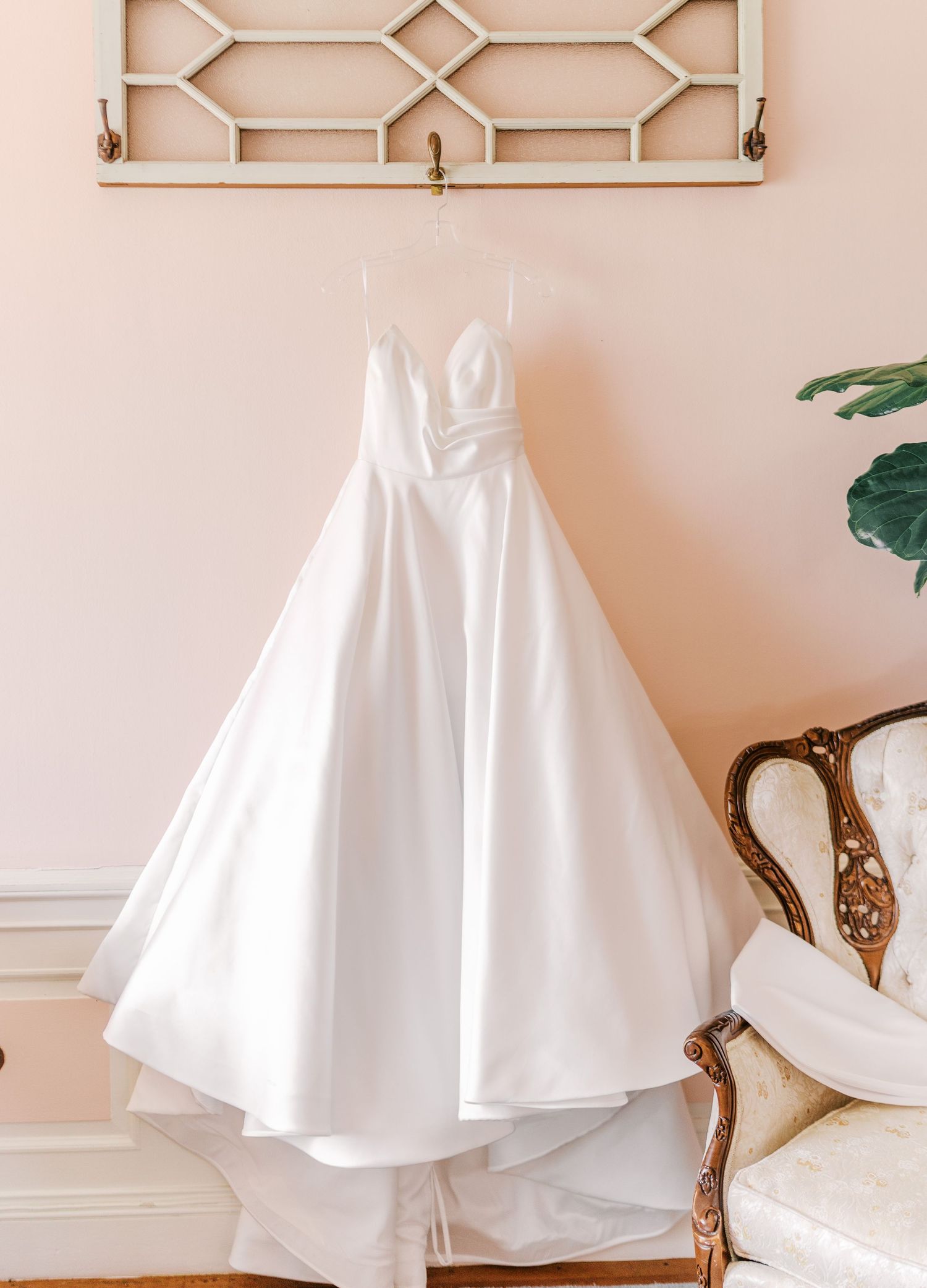 Elegant white ballgown wedding dress hanging on decorative wall with designer bridal shoes displayed nearby.