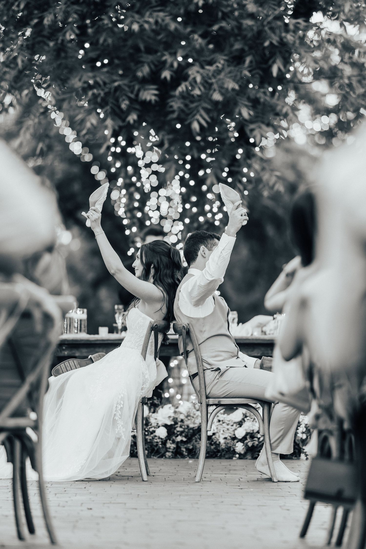 A playful outdoor wedding scene shows people dancing with twirls and spins under garden trees in black and white.