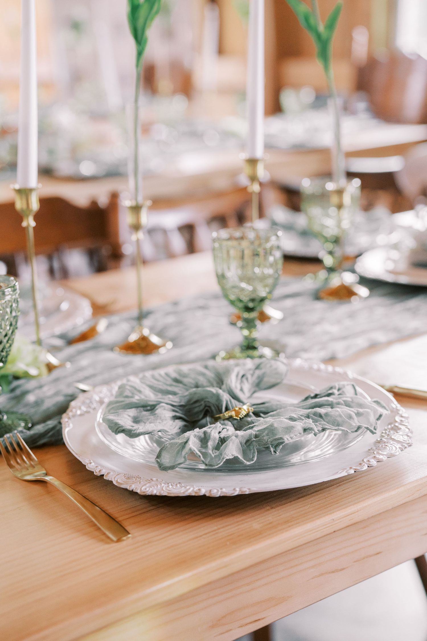 Elegant table setting with sage green napkins and ornate silver charger plates on a natural wood dining table.