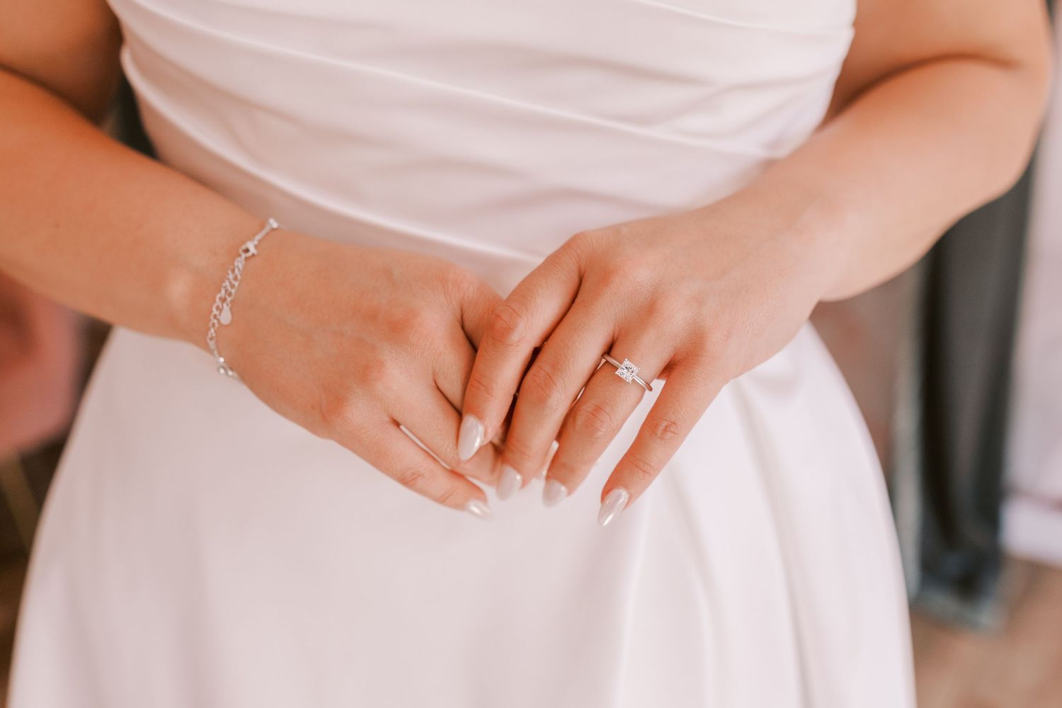 A close-up view of delicate bride hands wearing a white long sleeved wedding gown with floral lace details.