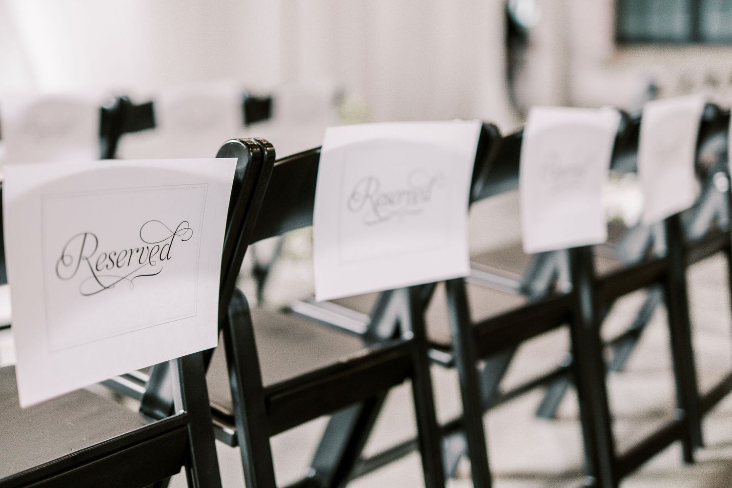 Reserved signs hang from black ceremony chairs in elegant calligraphy for a formal event.