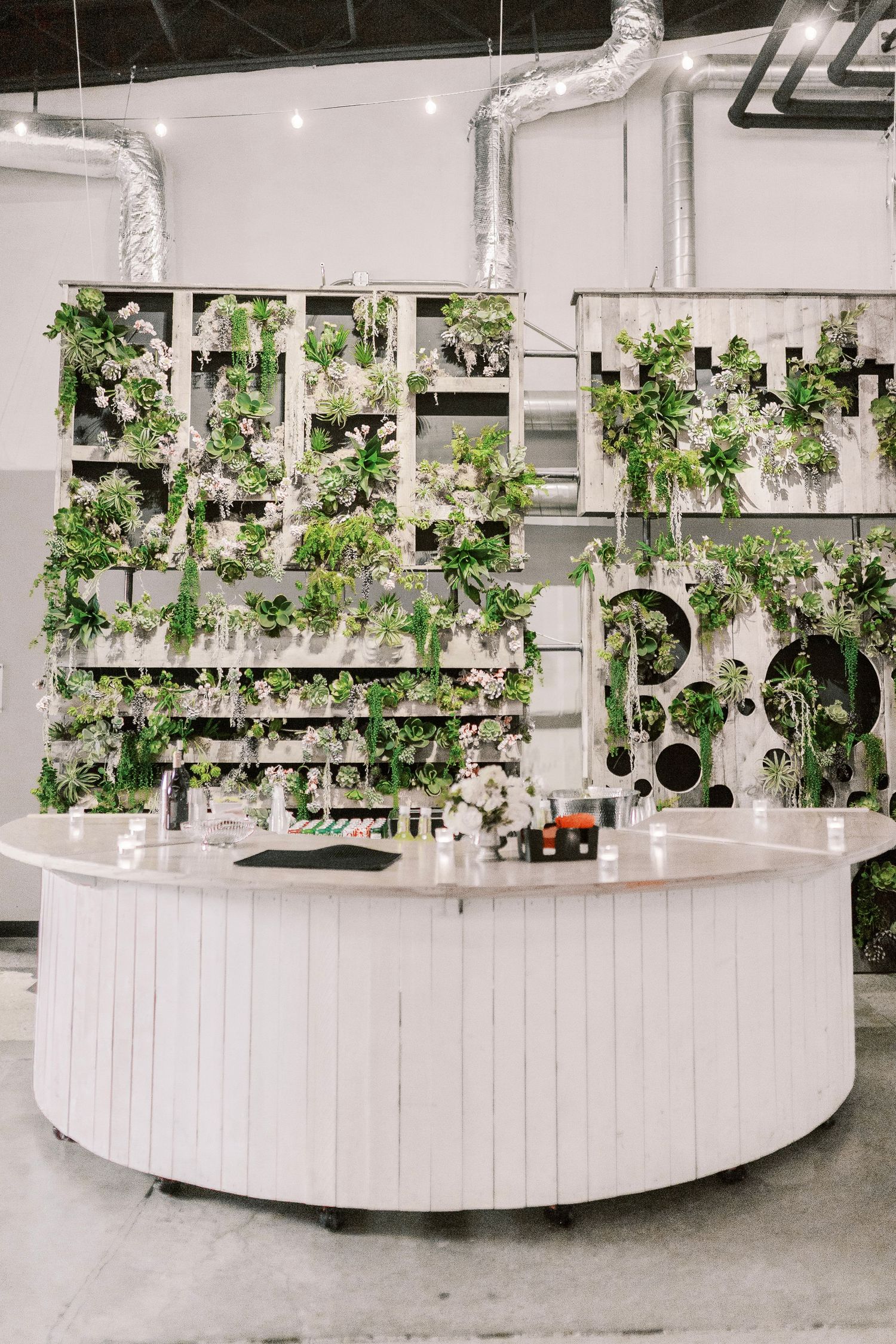 Modern white circular bar with lush green plant wall backdrop and industrial piping details.