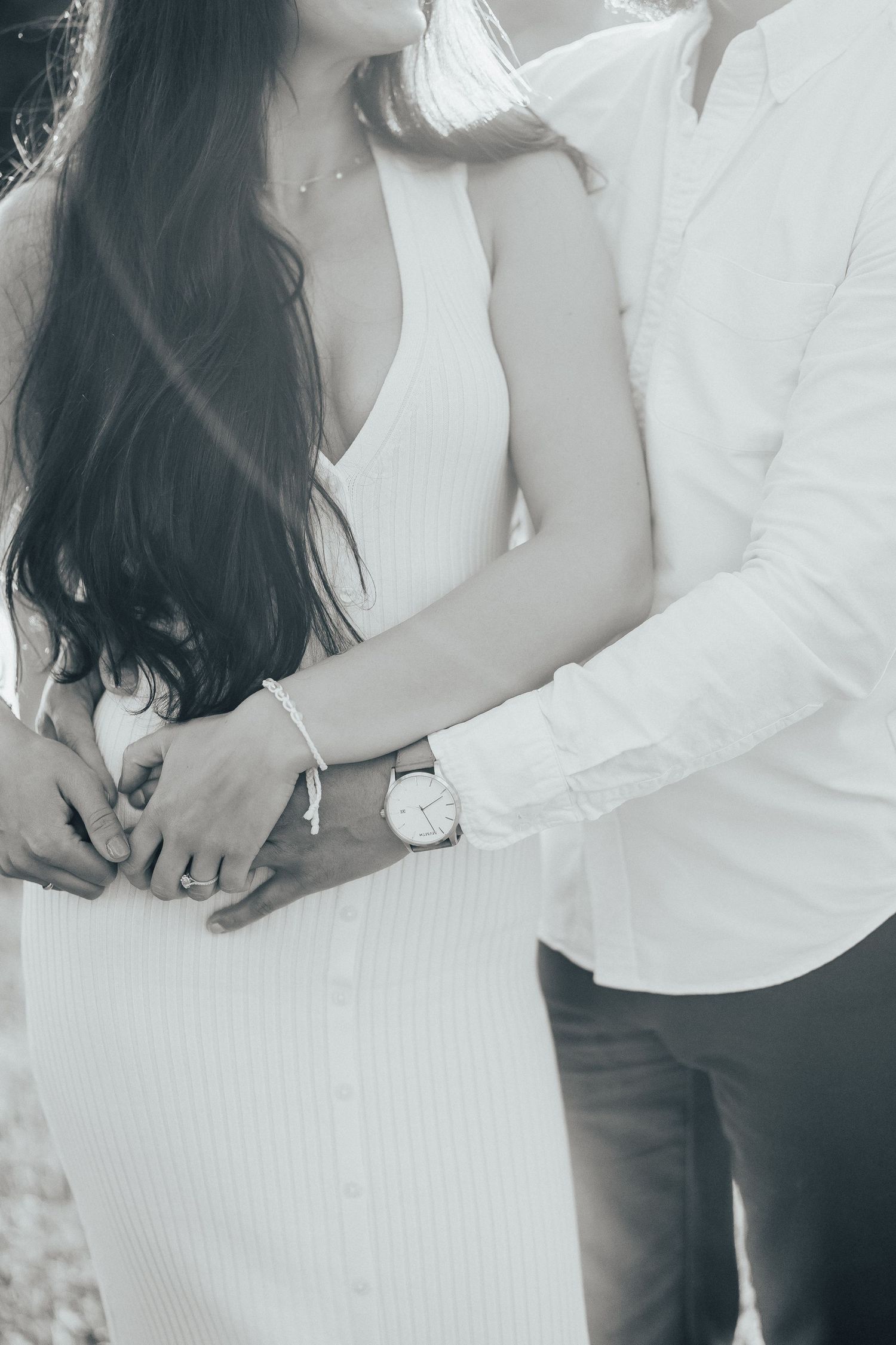 Close up of a couple in white outfits holding hands, with long dark hair and a watch visible.