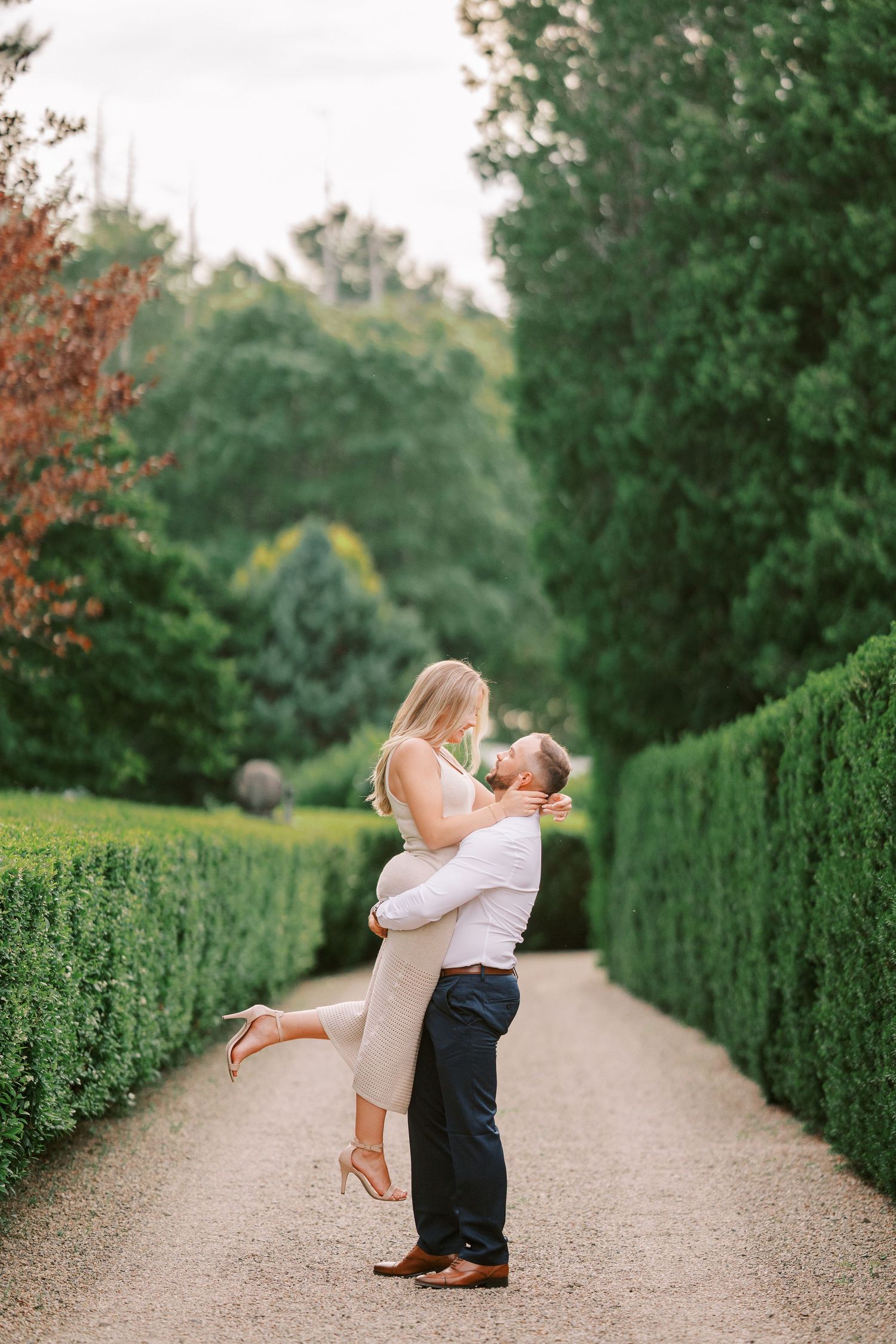 Couple sharing intimate moment on garden path lined with manicured hedges.