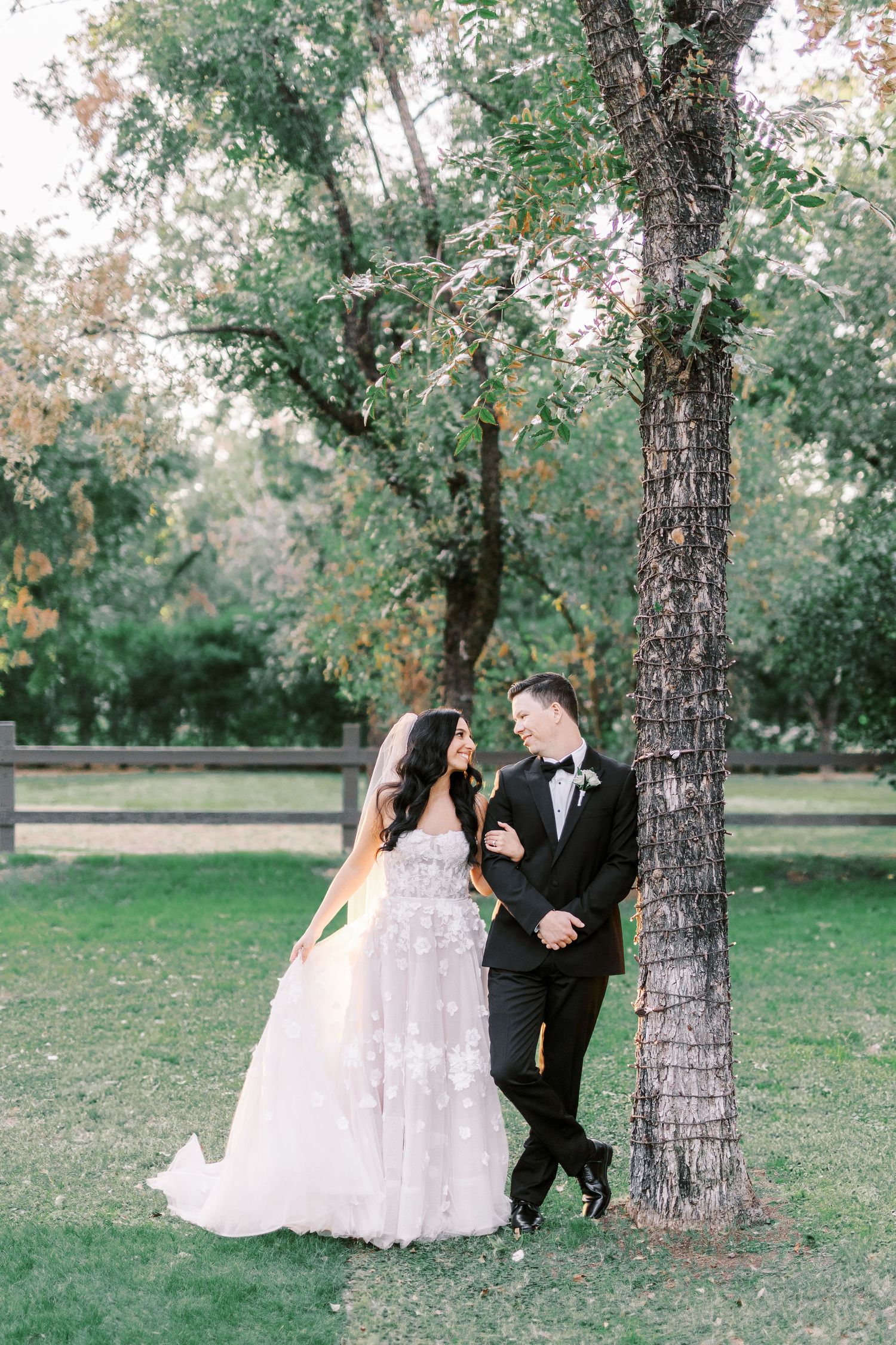 A couple shares a romantic moment under a tree during their outdoor wedding photoshoot in a serene garden setting.