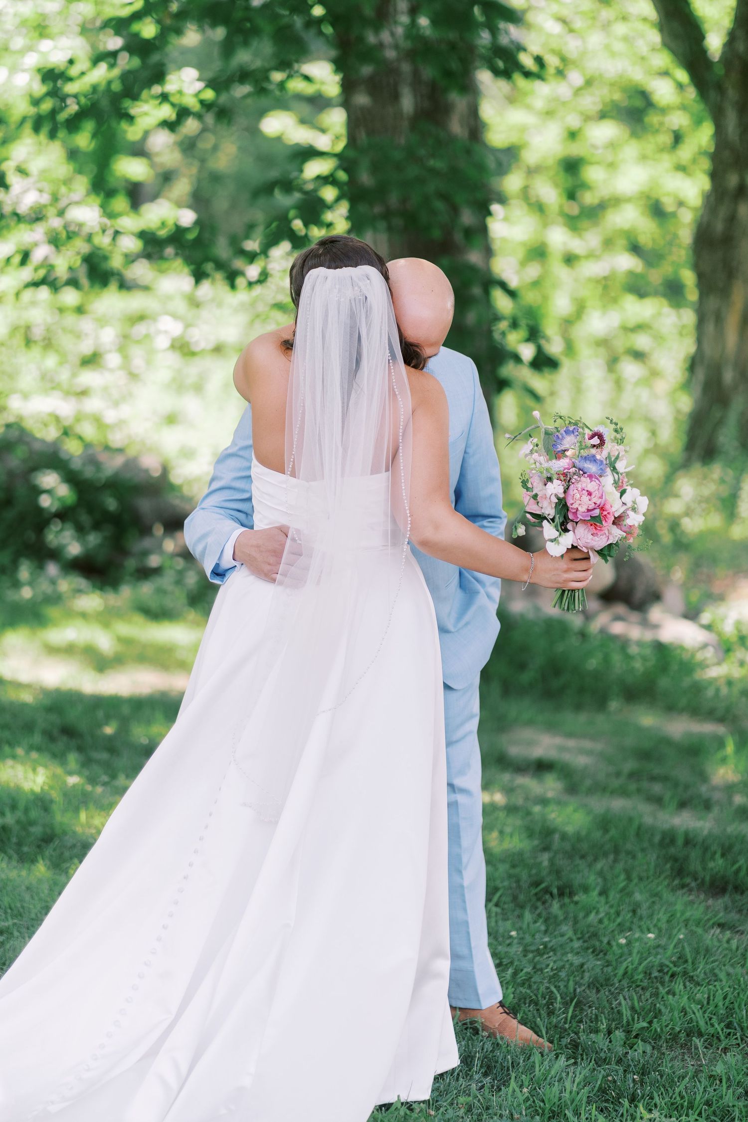 Wedding couple embracing in a lush garden setting with a flowing white dress and colorful bouquet.