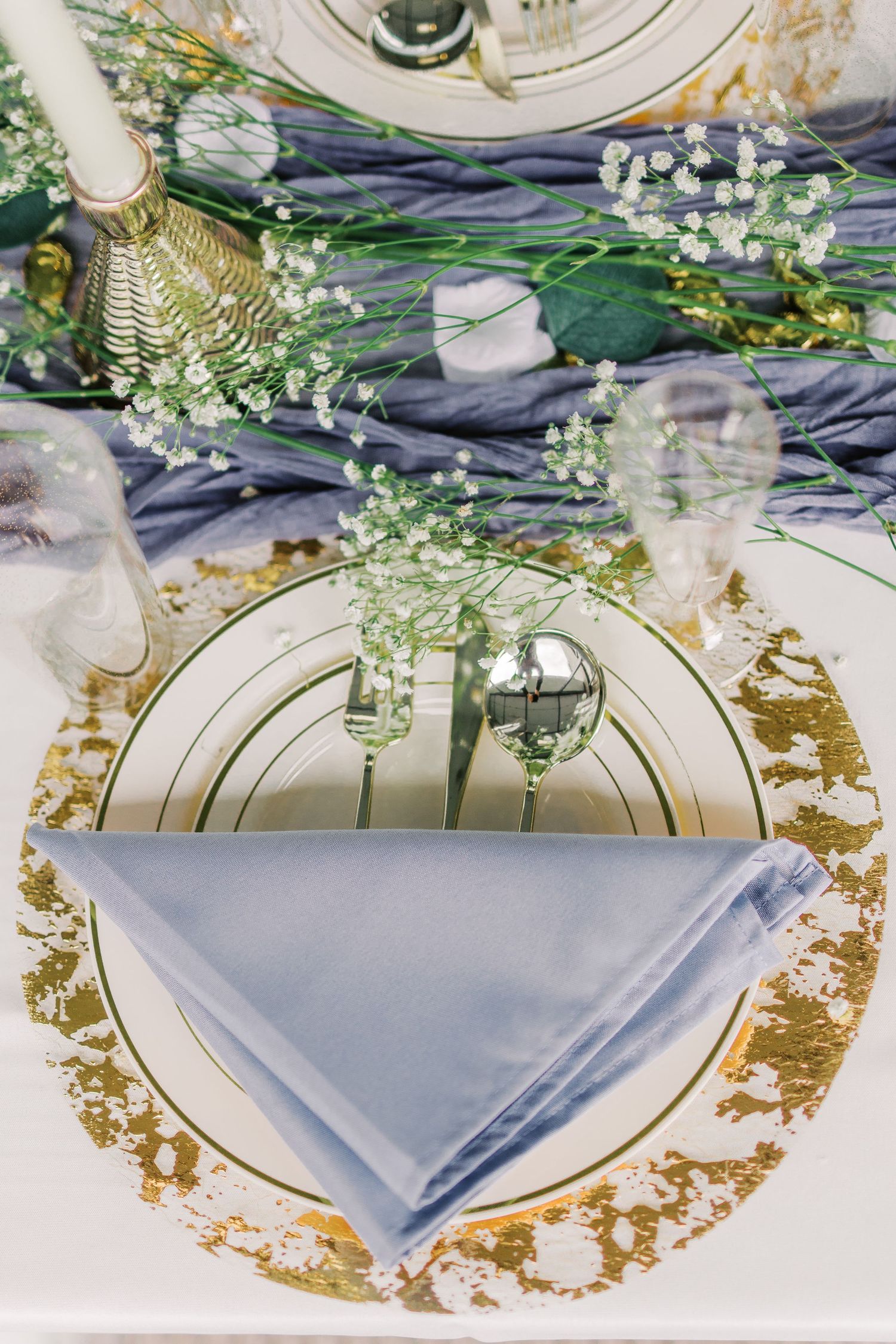 Elegant place setting with gold charger plate, blue napkin and baby's breath decor.