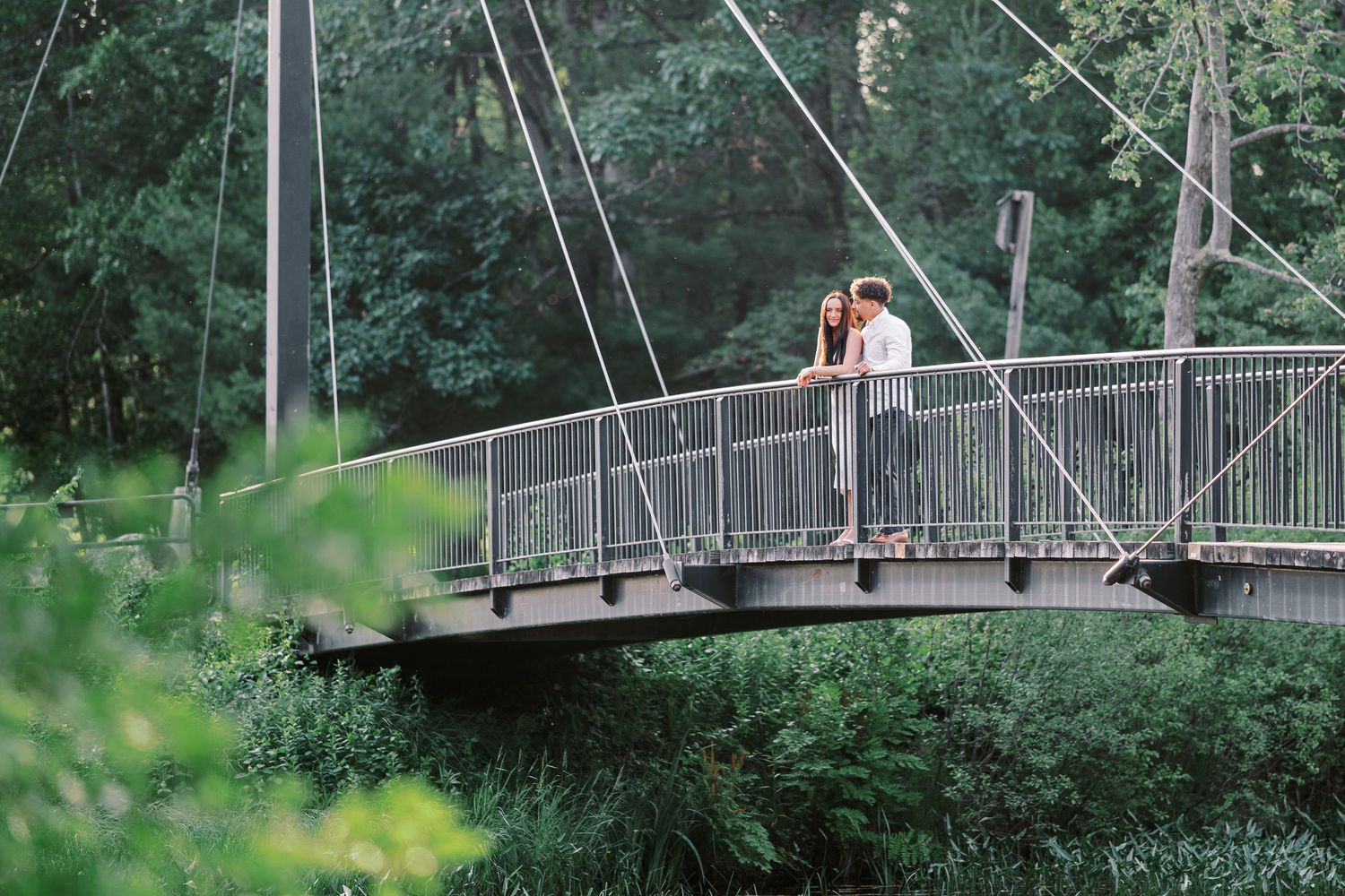 Modern pedestrian bridge spanning across a lush green landscape surrounded by trees.