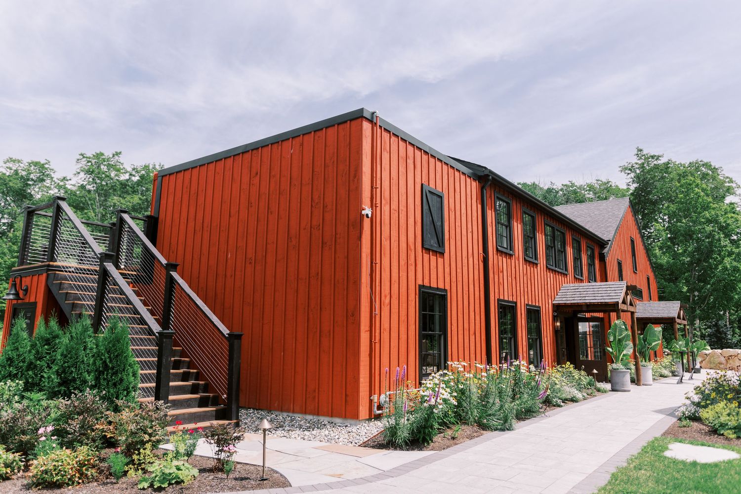 Modern red barn-style building with exterior stairs and landscaped garden path under overcast sky.