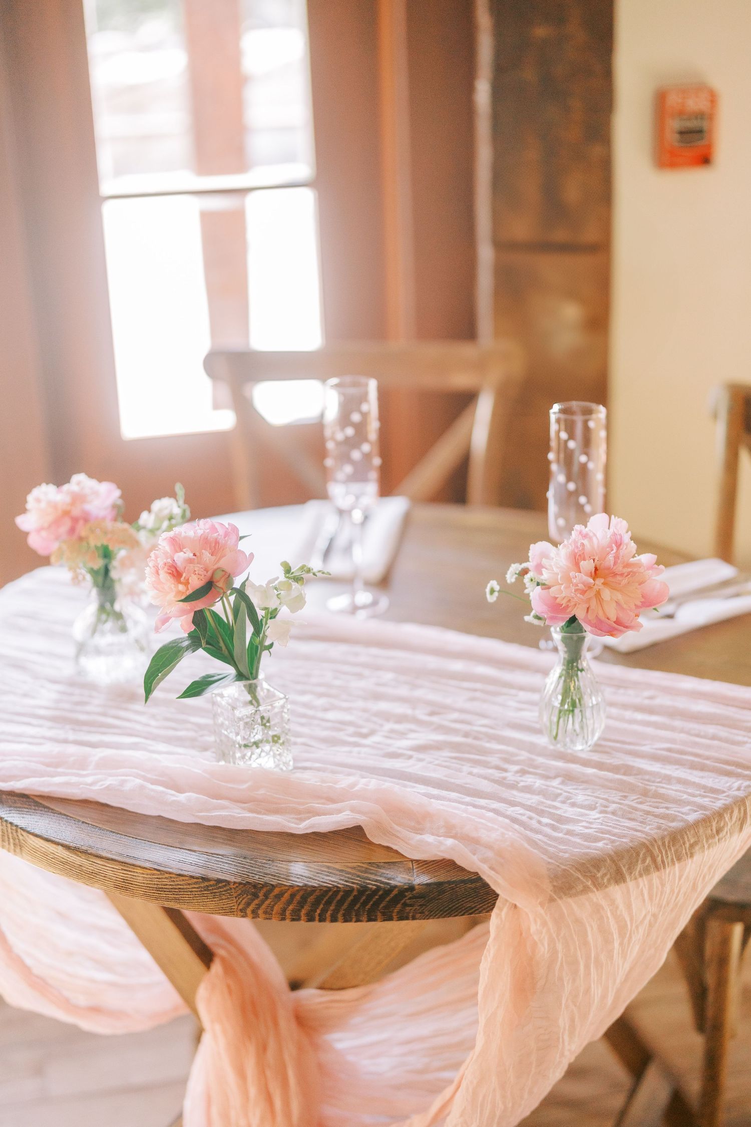 Table setting with pink flowers in vases and blush linens for an elegant wedding reception.