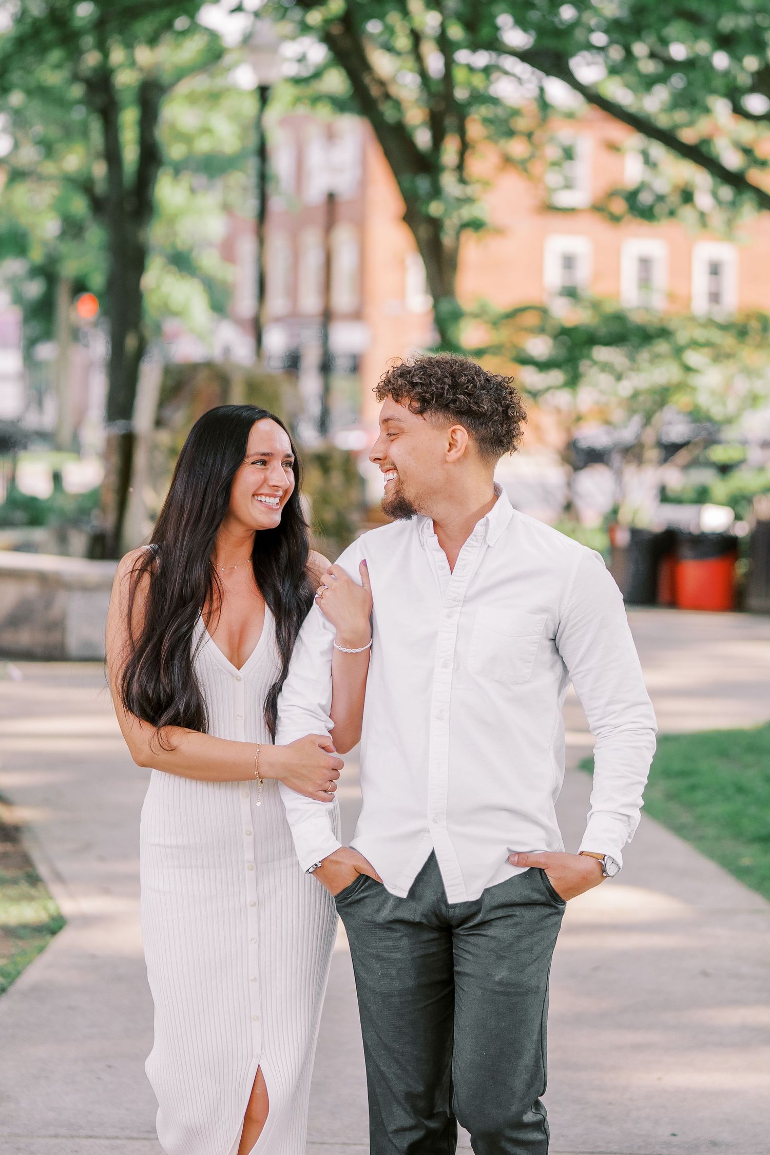 A couple shares playful moments while walking in a tree-lined park pathway.