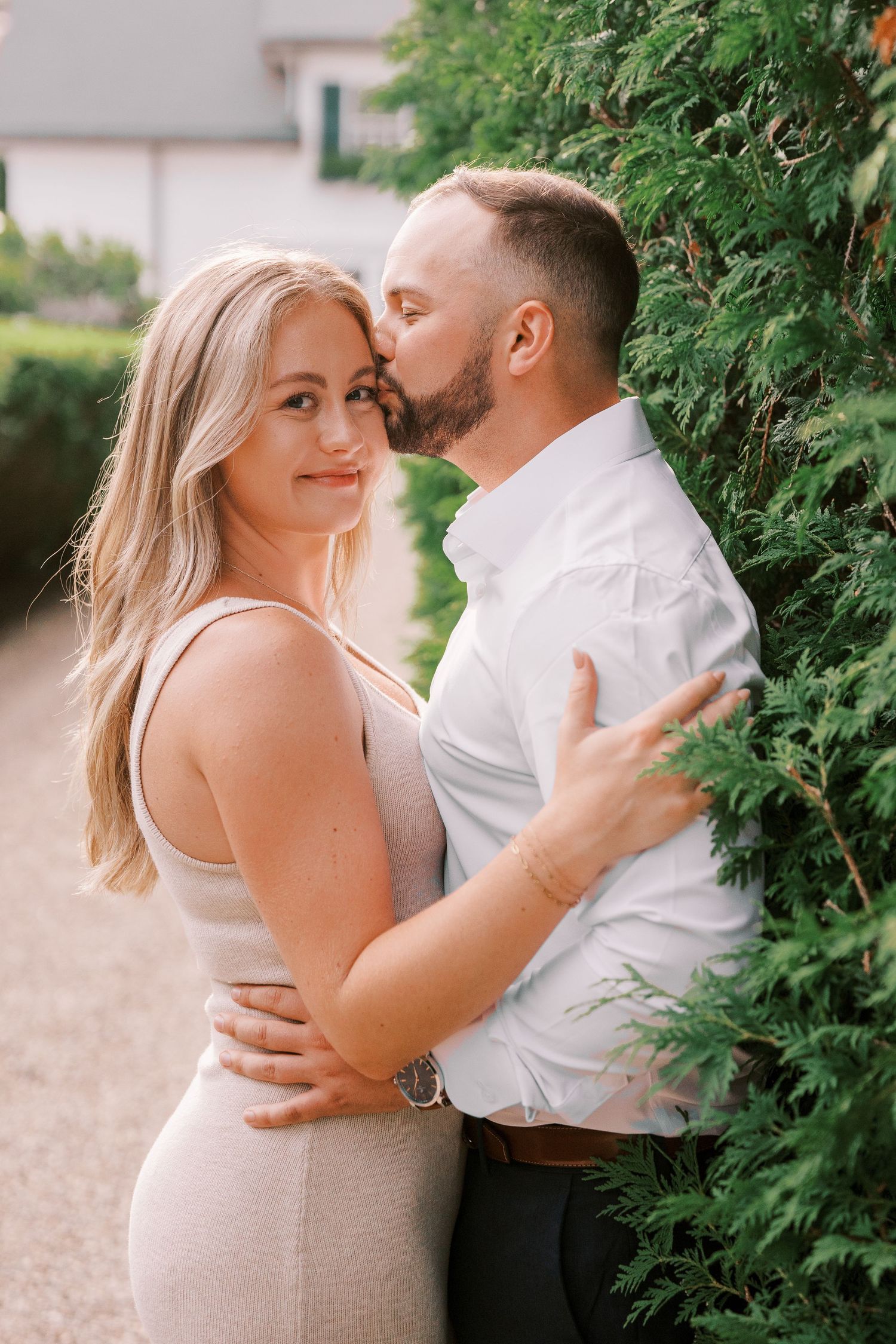Romantic couple embracing against green foliage in outdoor garden setting during engagement photoshoot.