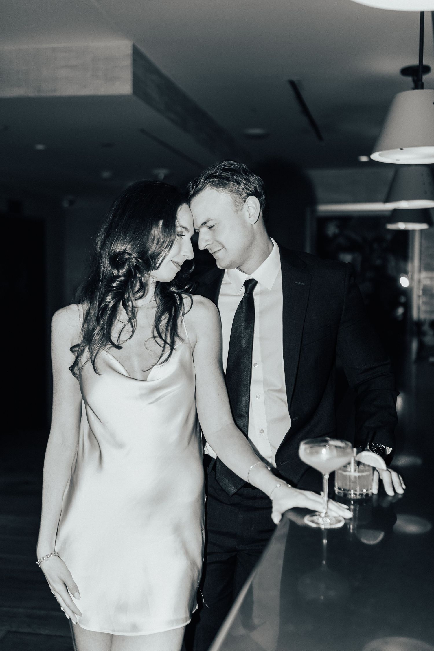 Romantic black and white photo of a couple in formal wear sharing an intimate moment at a dimly lit bar.