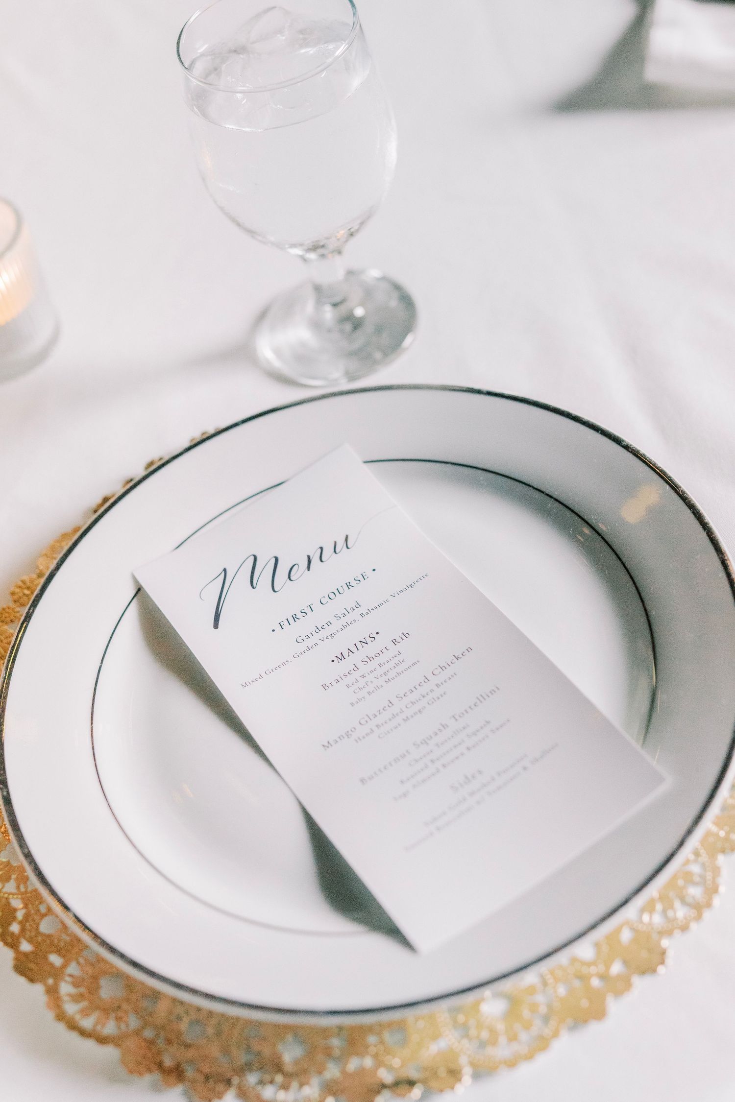 Wedding place setting with elegant menu card on gold charger plate and white china.