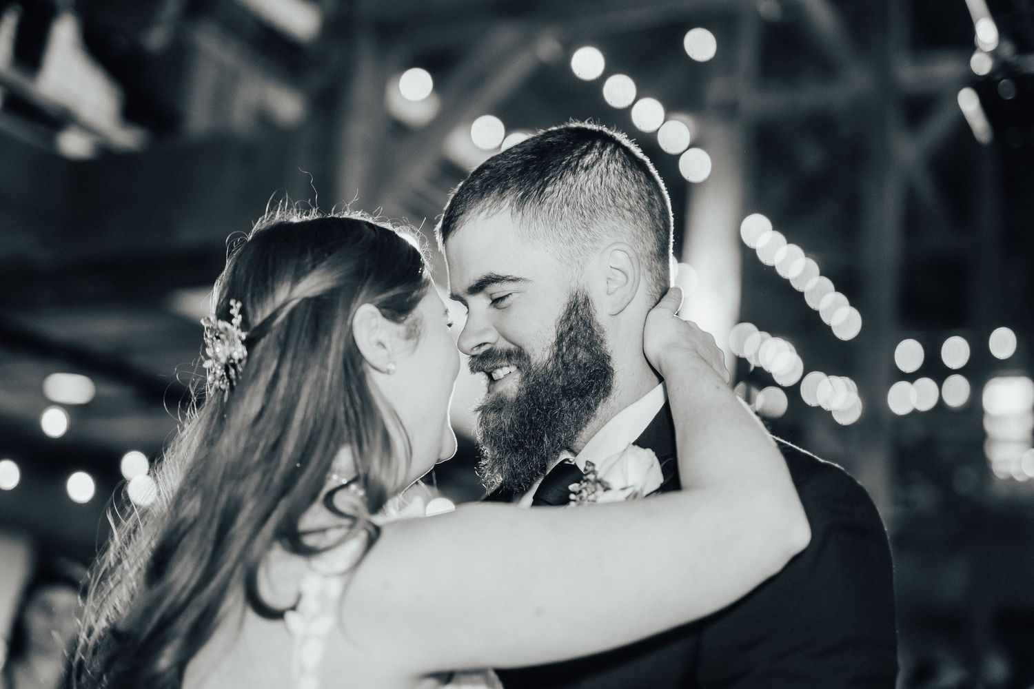 Close-up black and white photo of couple sharing intimate dance moment under twinkling lights.