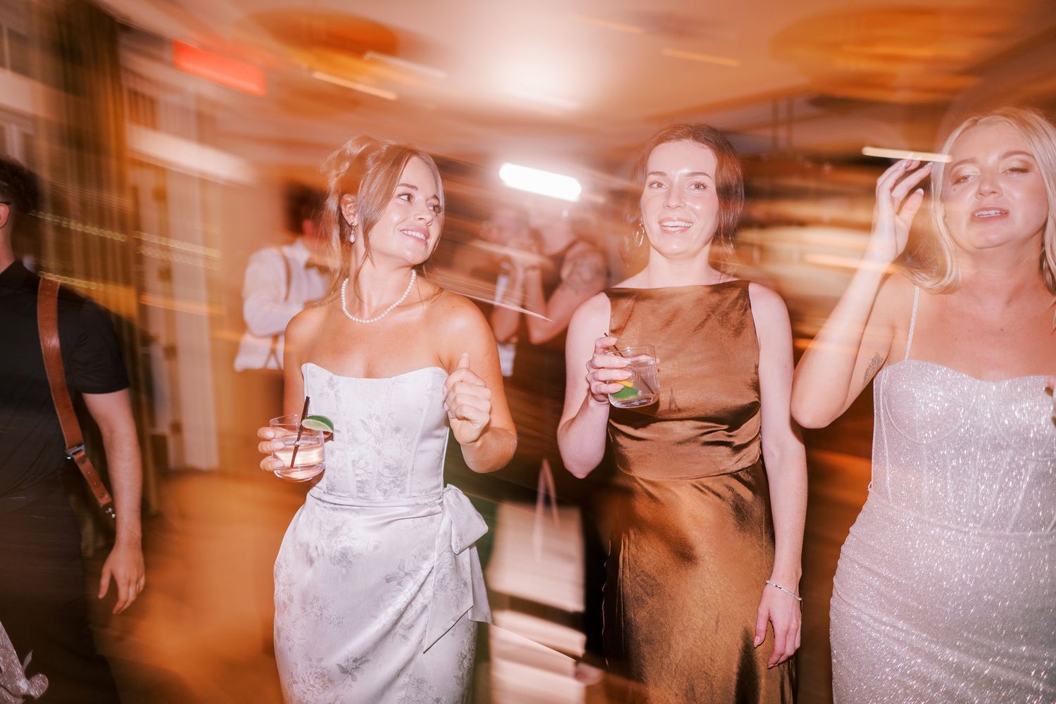 Motion-blurred party scene showing people dancing and laughing at a celebration, with orange-tinted lighting effects.
