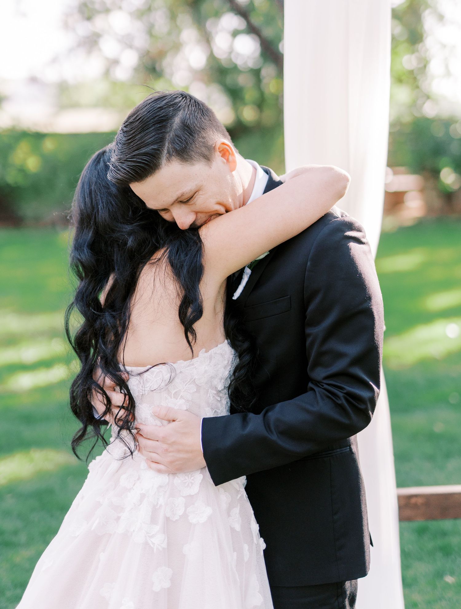 A romantic candid moment of a couple in formal wedding attire embracing outdoors near white columns.