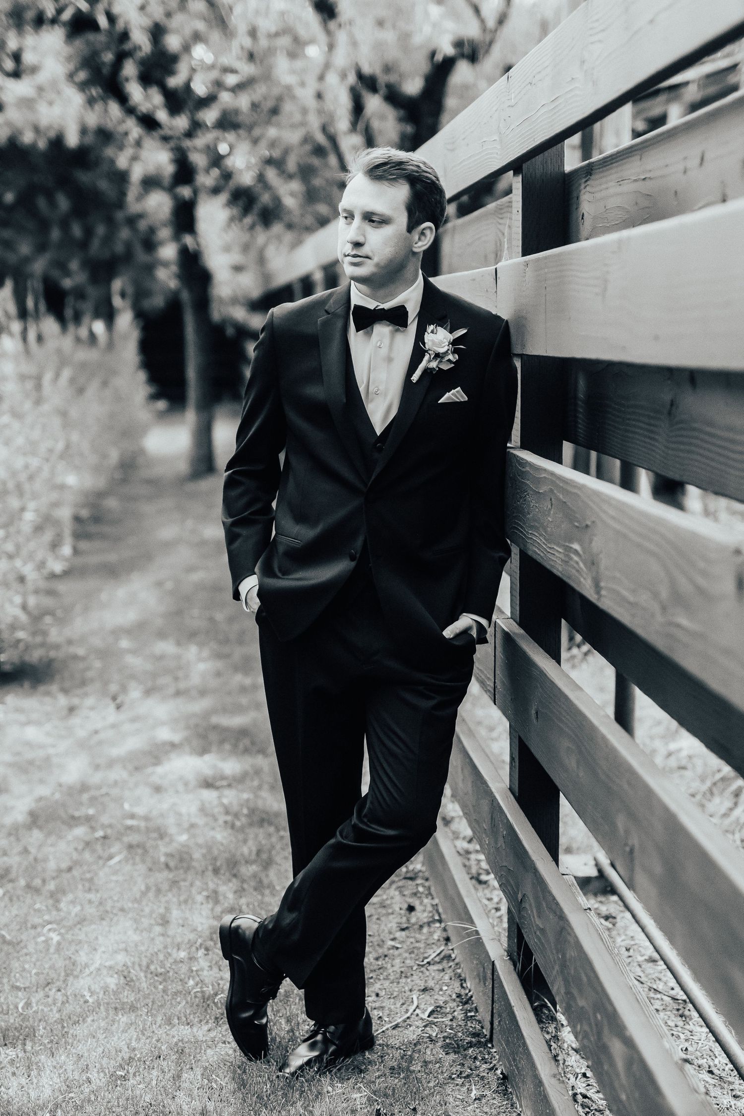 A series of black and white photos showing someone in a formal suit leaning against a wooden fence in an outdoor setting.