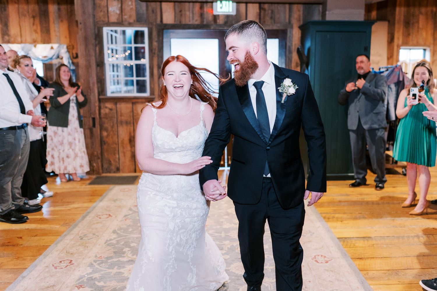 A joyful couple makes their grand entrance in a rustic wooden venue surrounded by guests.