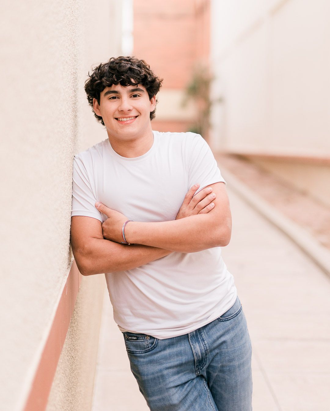 A person wearing a white t-shirt and blue jeans poses casually against a pastel pink background.
