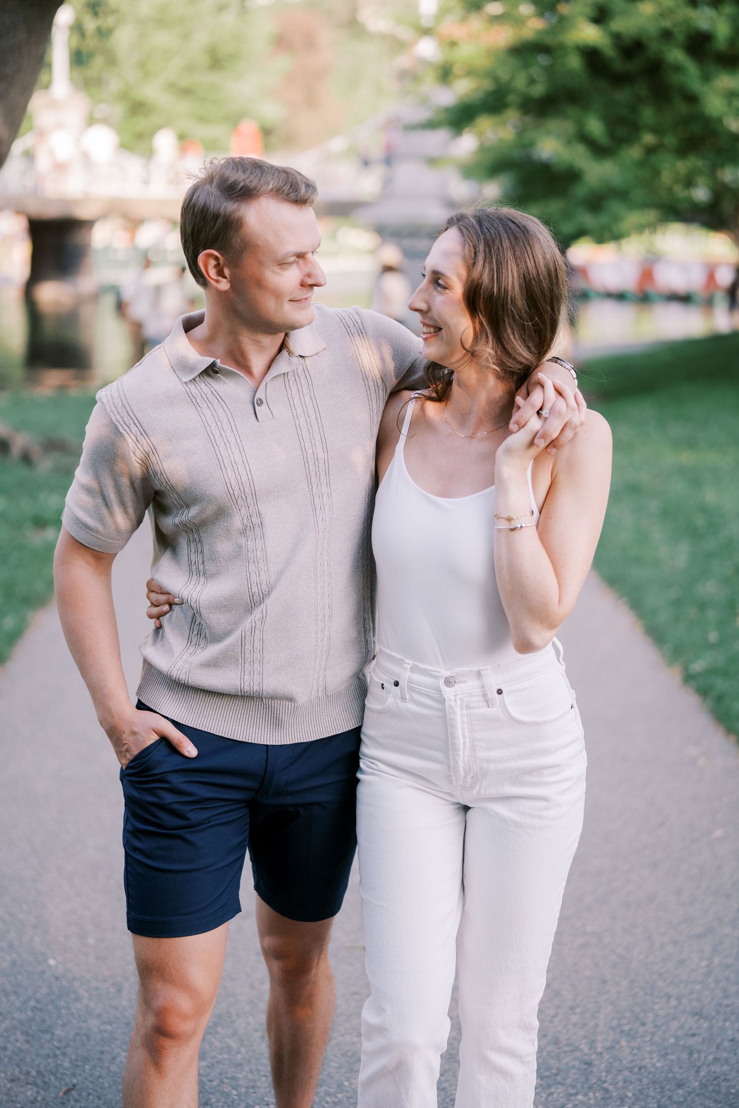 A couple laughing and walking together in a park wearing casual summer outfits.