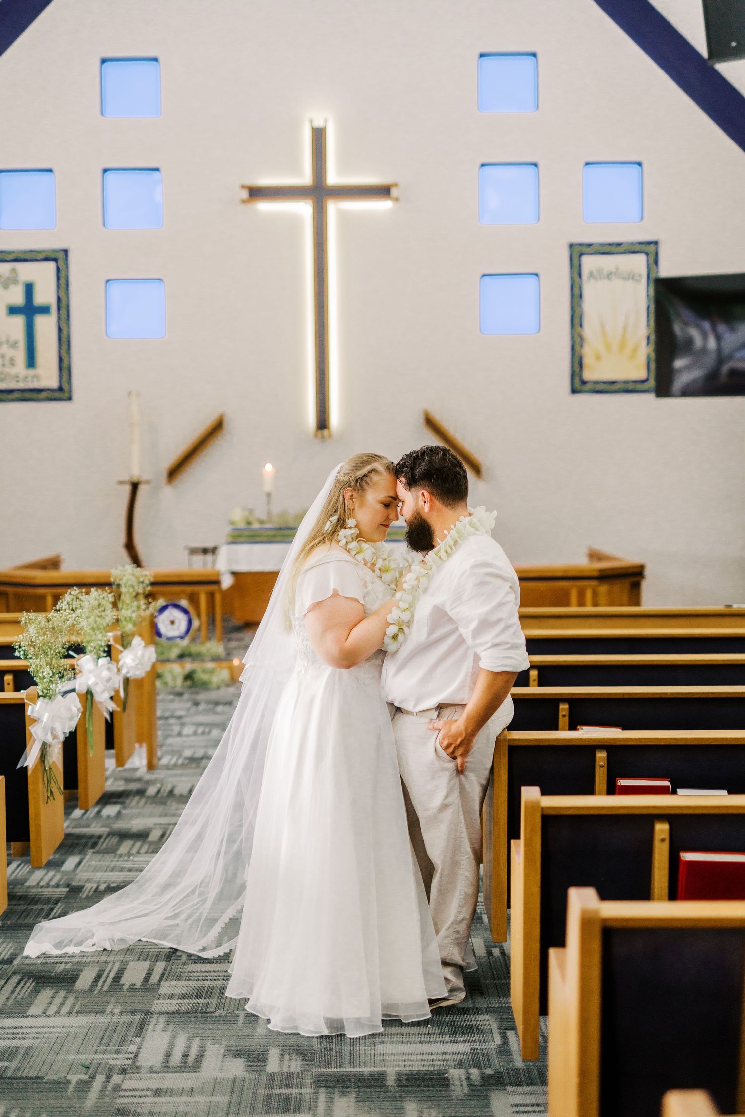 A couple shares an intimate moment in a church with a glowing cross in the background.