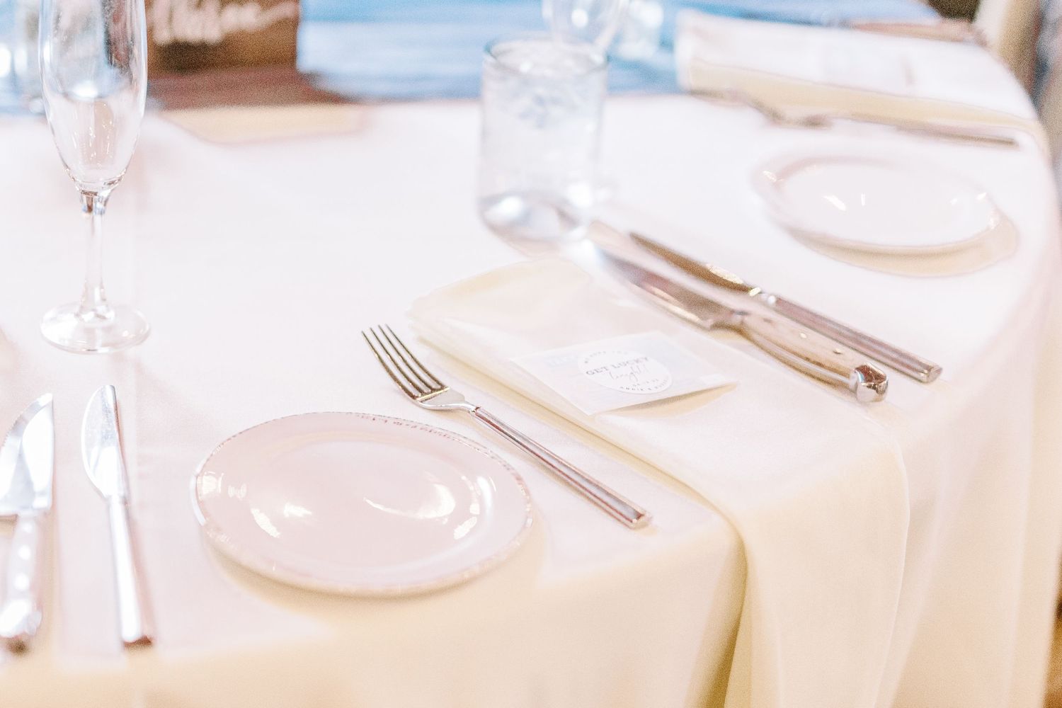 Elegant place setting with white plates, silverware, and wine glasses on a crisp linen tablecloth.