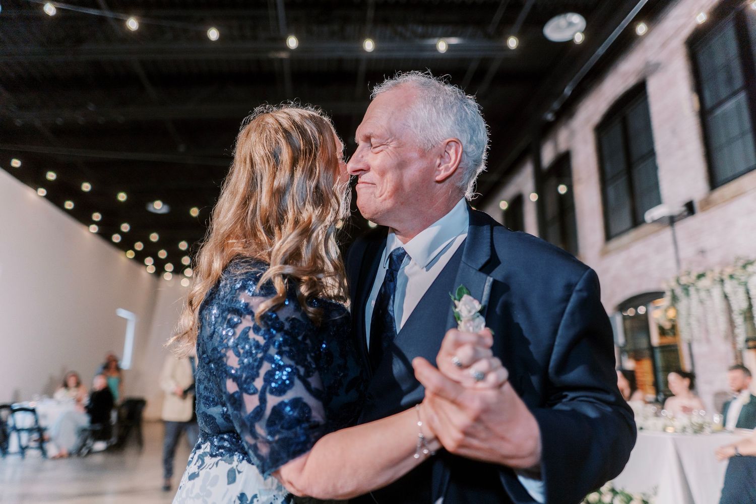 Couple dancing at wedding reception under string lights in an elegant venue.
