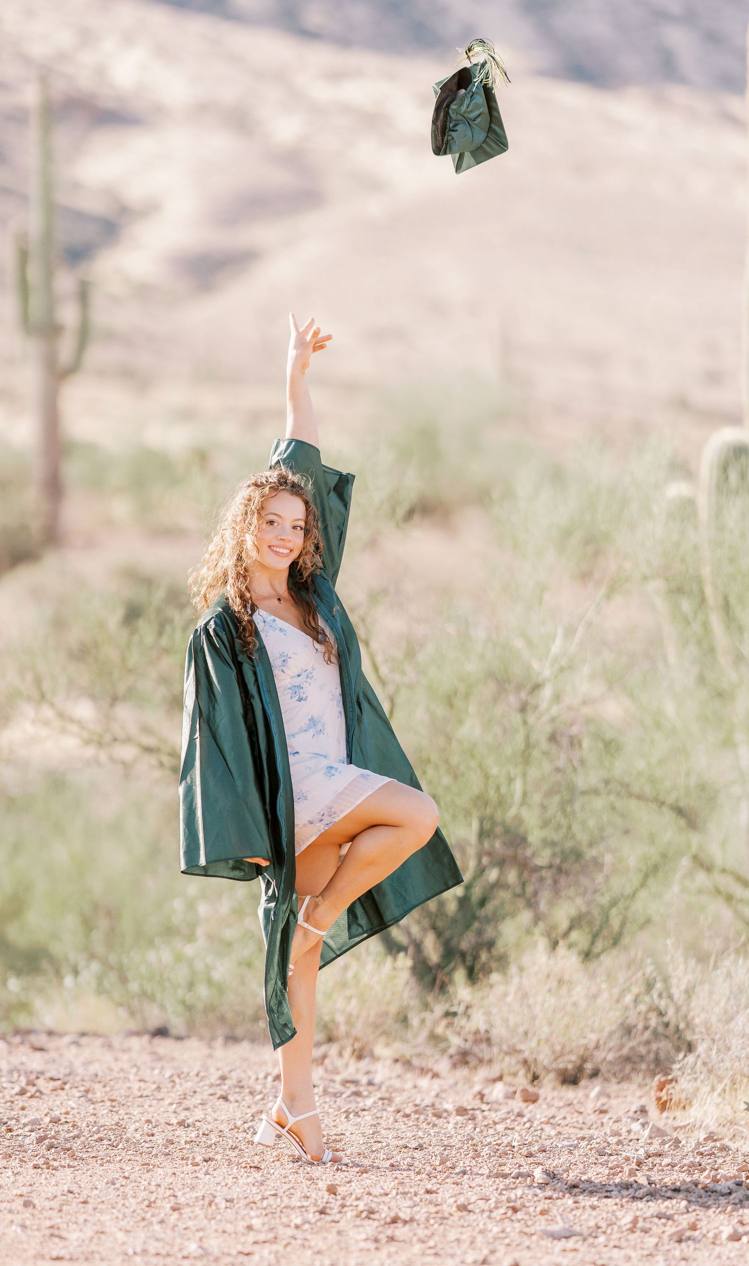 A graduate in orange pants and green gown playfully throws their cap in three sequential photos in a desert setting.