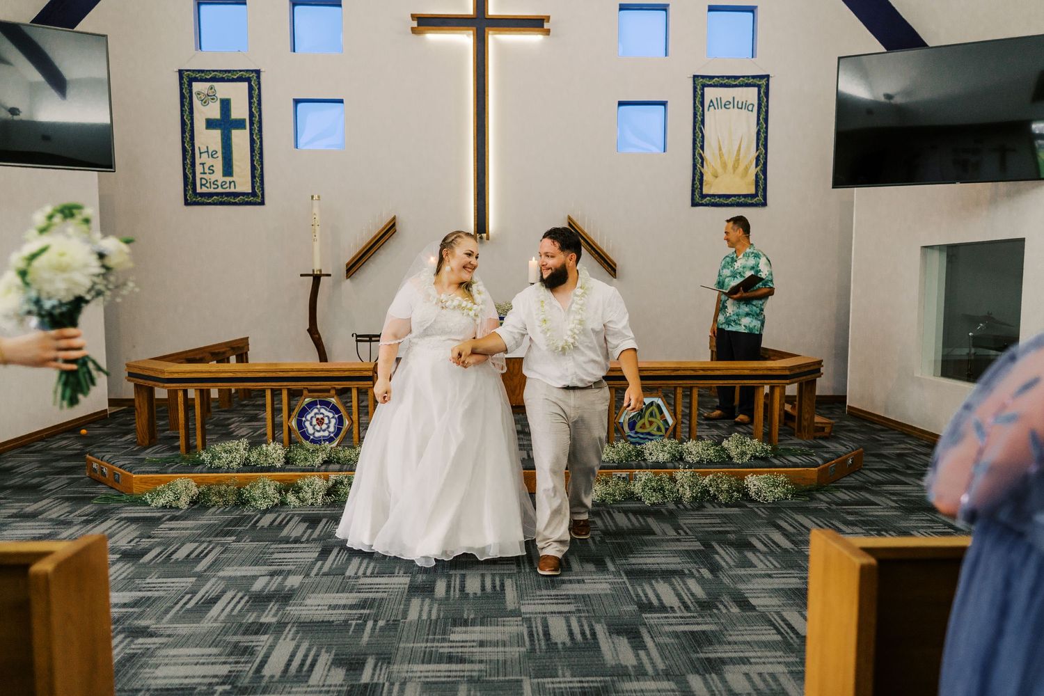 A couple celebrates at the altar in a modern church with a large cross and windows.
