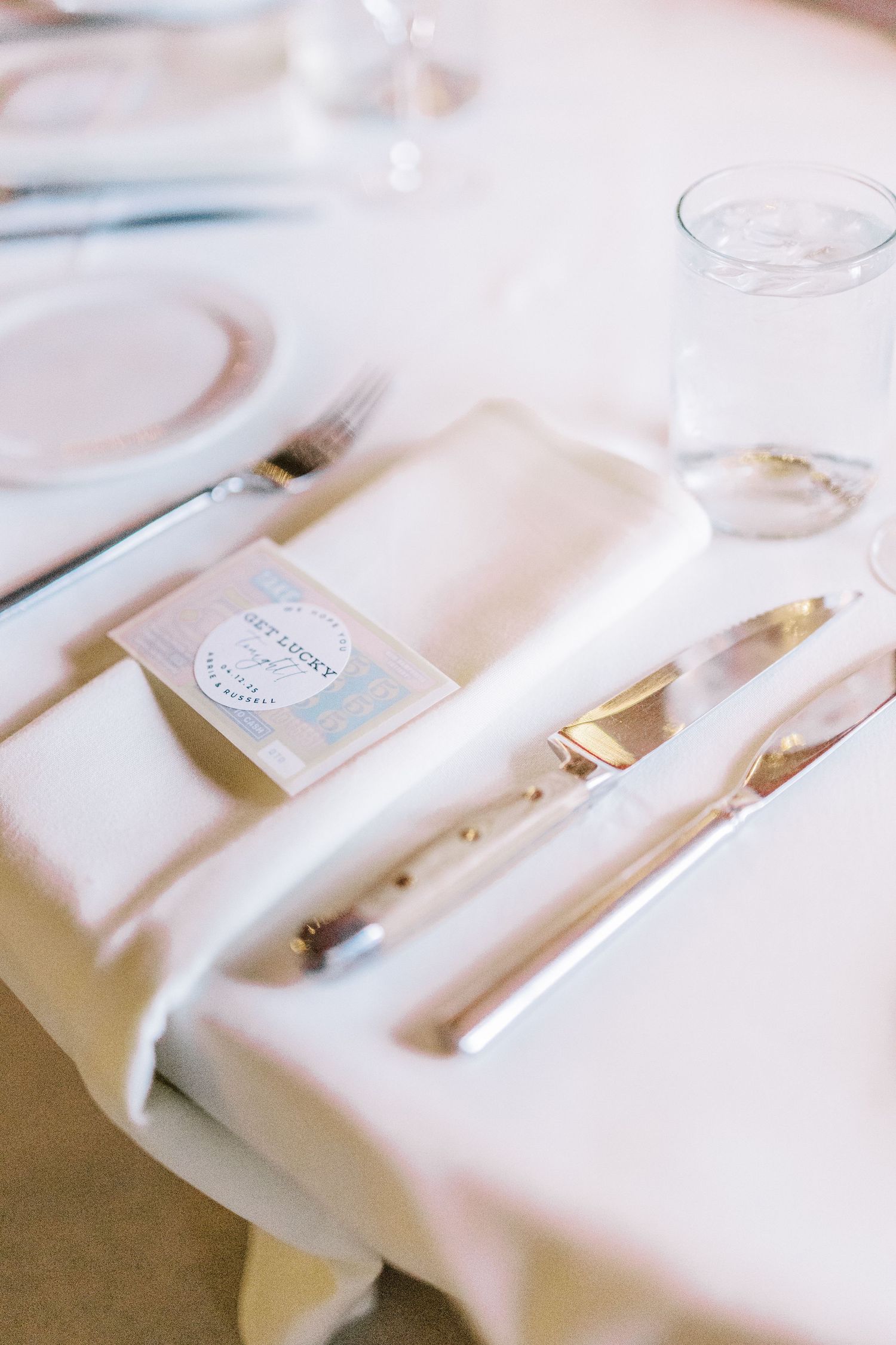 Elegant white place setting with napkin, silverware and name card on a wedding reception table.