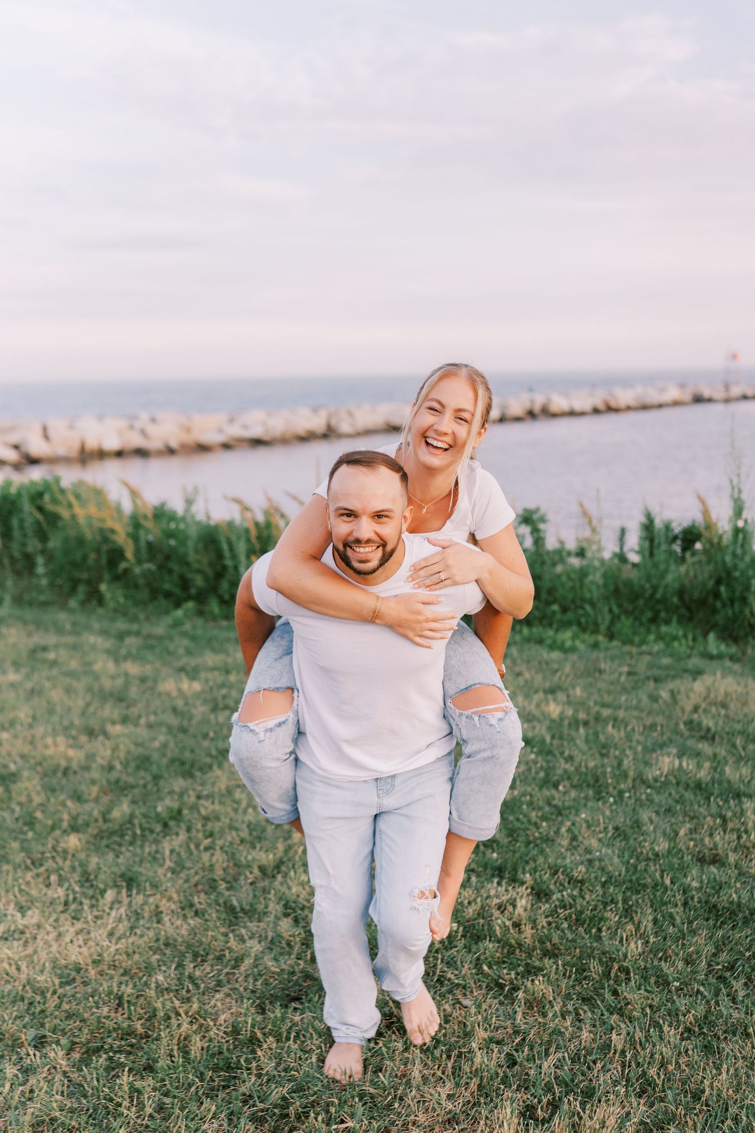 A joyful couple shares a piggyback ride by the waterfront at sunset.