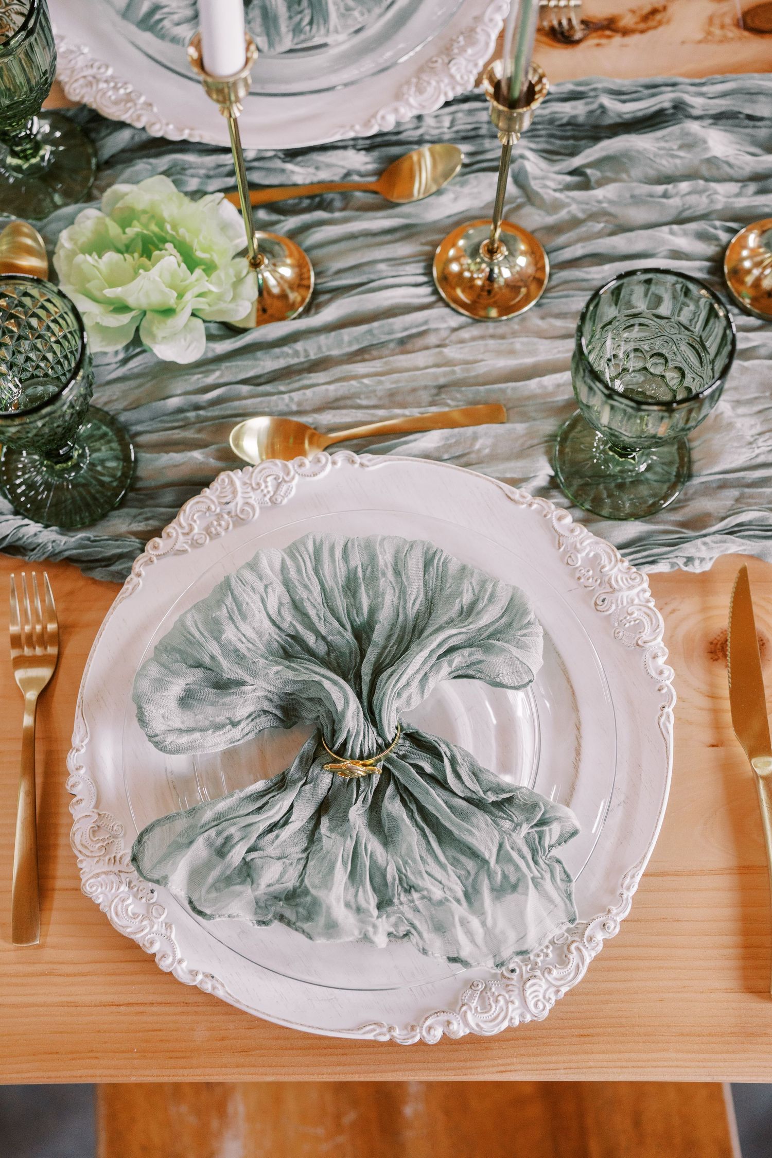 Elegant table setting with gray napkin artfully folded on ornate white plate with green glassware and floral accents.