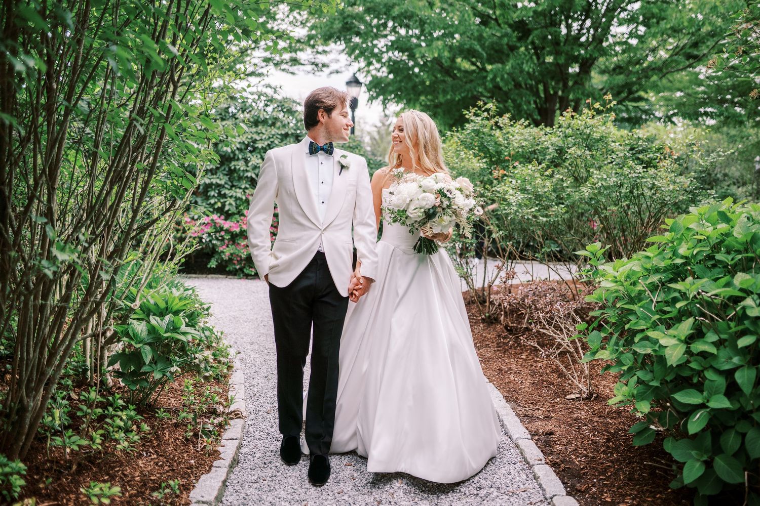 A wedding couple walks along a lush garden path surrounded by greenery.