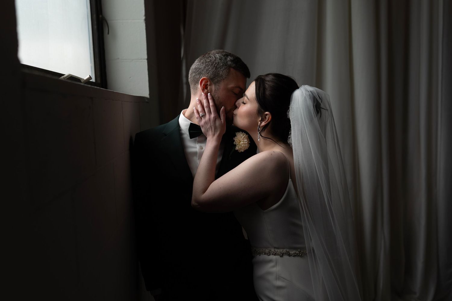 Intimate wedding portrait of couple sharing a tender moment in dramatic lighting.