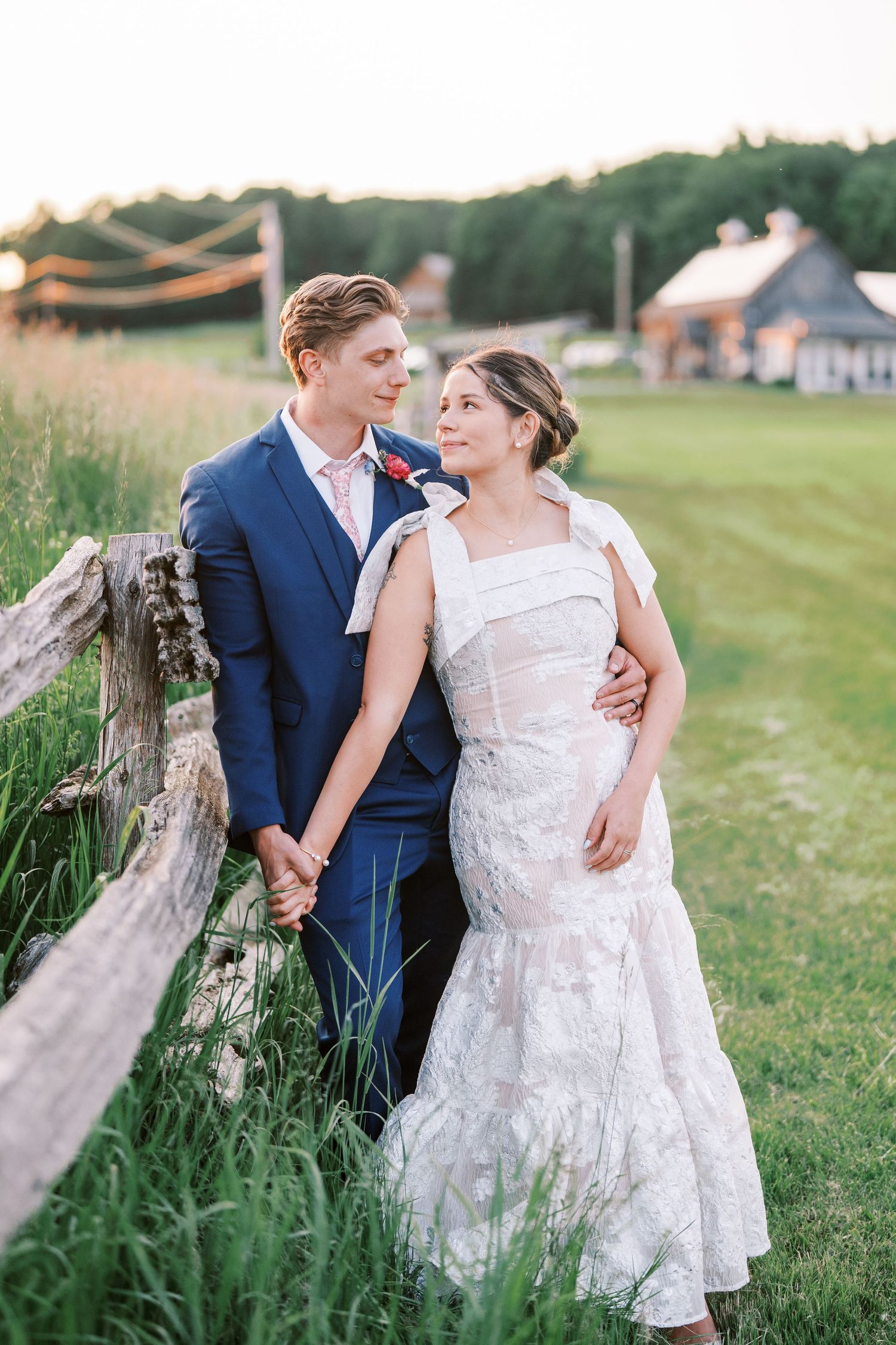 Newlywed couple shares romantic moments together in a grassy field during their outdoor summer photoshoot.
